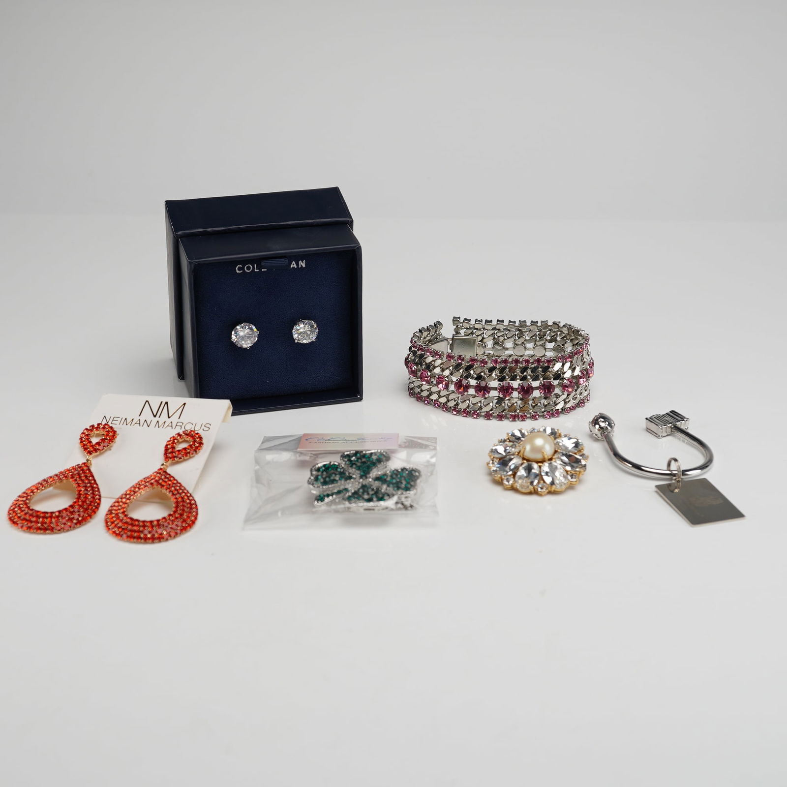 A Collection of Six Costume Jewelry Pieces and Branded Accessories: A collection of six costume jewelry pieces and accessories. The lot includes one wide, articulated silver-tone bracelet densely set with multiple rows of pink/ruby-toned rhinestones. There are two pai