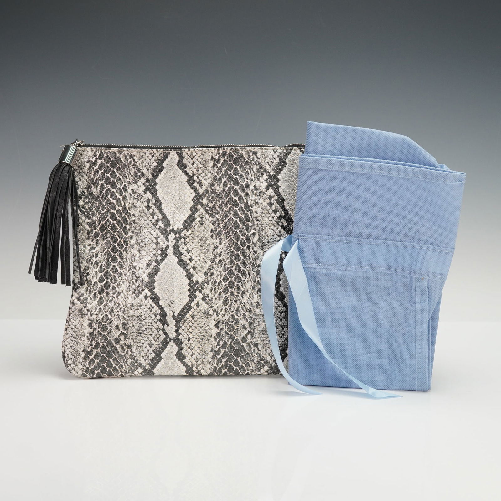 A Bergdorf Goodman Embossed Faux Snakeskin Clutch and Dust Bag: A Bergdorf Goodman embossed faux snakeskin clutch bag. The rectangular contemporary clutch features a pattern in shades of black, grey, and off-white, secured with a silver-toned metal zipper. A