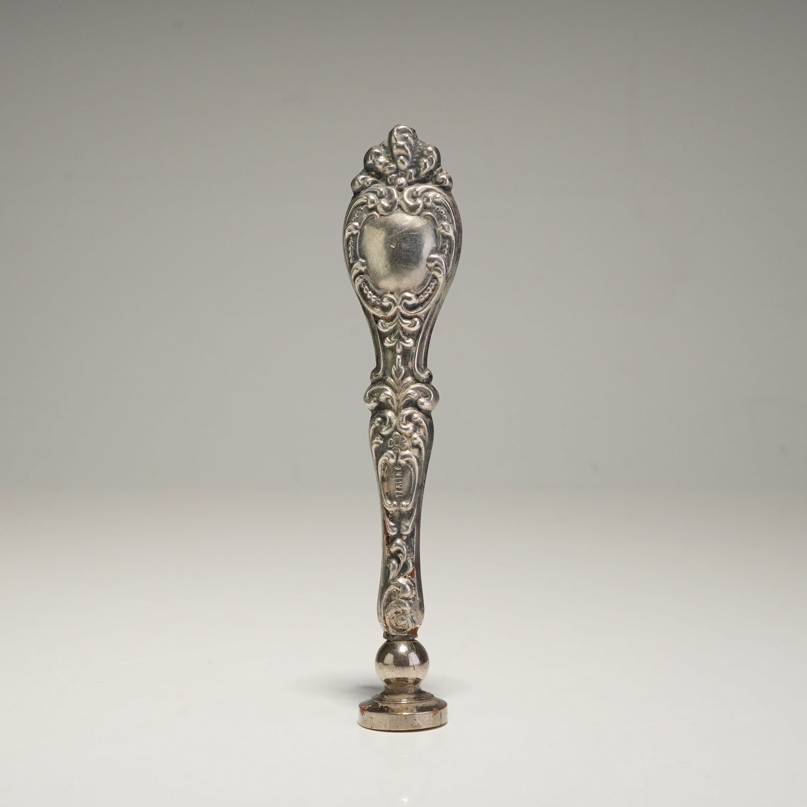 Sterling Silver Repousse Wax Seal Stamp: This ornate sterling silver wax seal stamp features a handle decorated with repousse scrollwork and floral motifs centered around a shield-shaped cartouche. The handle is marked with an impressed STER