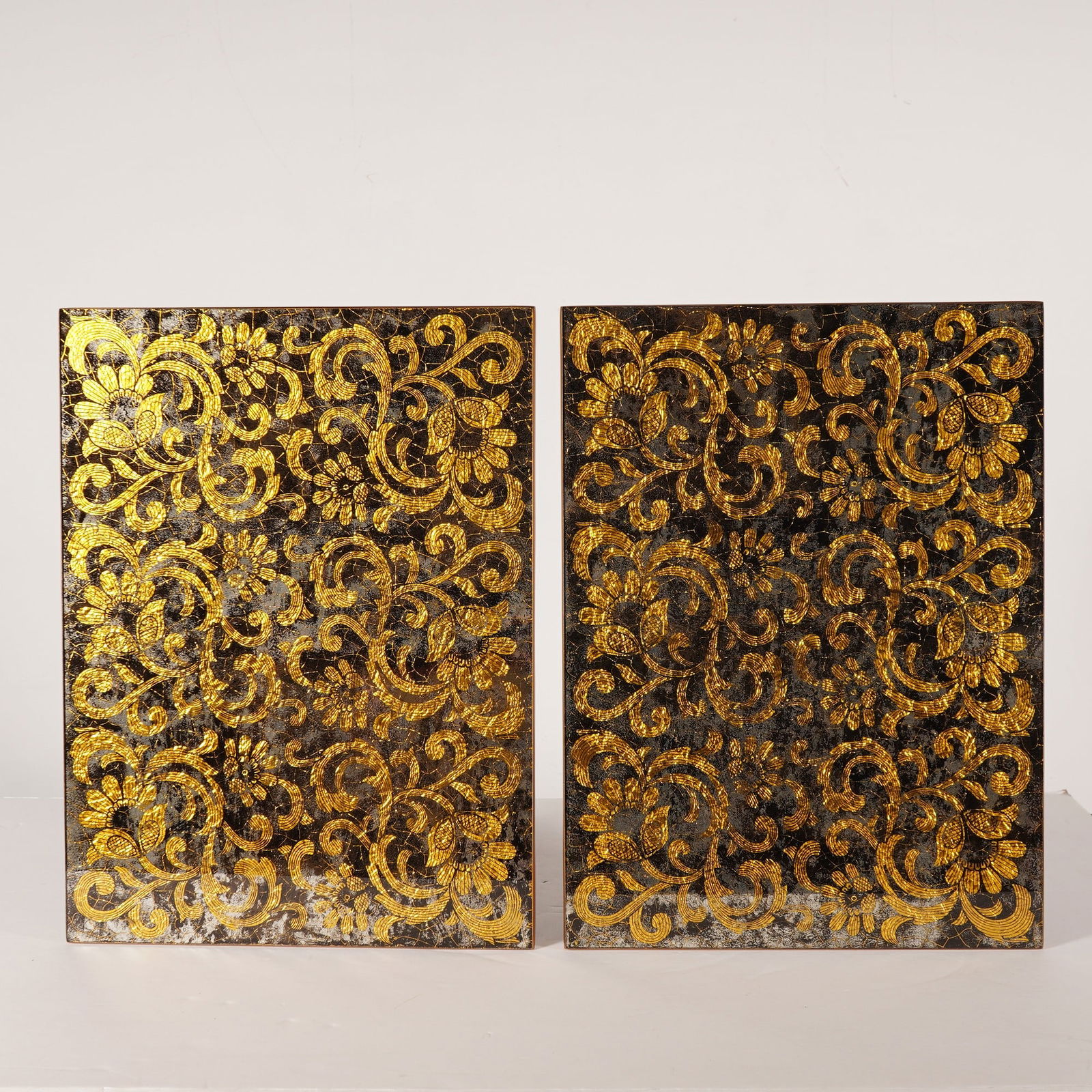 2pc Nomi K Black and Gold Glass Lace Motif Mirror Placemats: A pair of Nomi K glass placemats featuring a black and gold lace motif with gold leaf detailing. Each rectangular panel is decorated with an ornate floral and scrollwork design against a dark, heavily