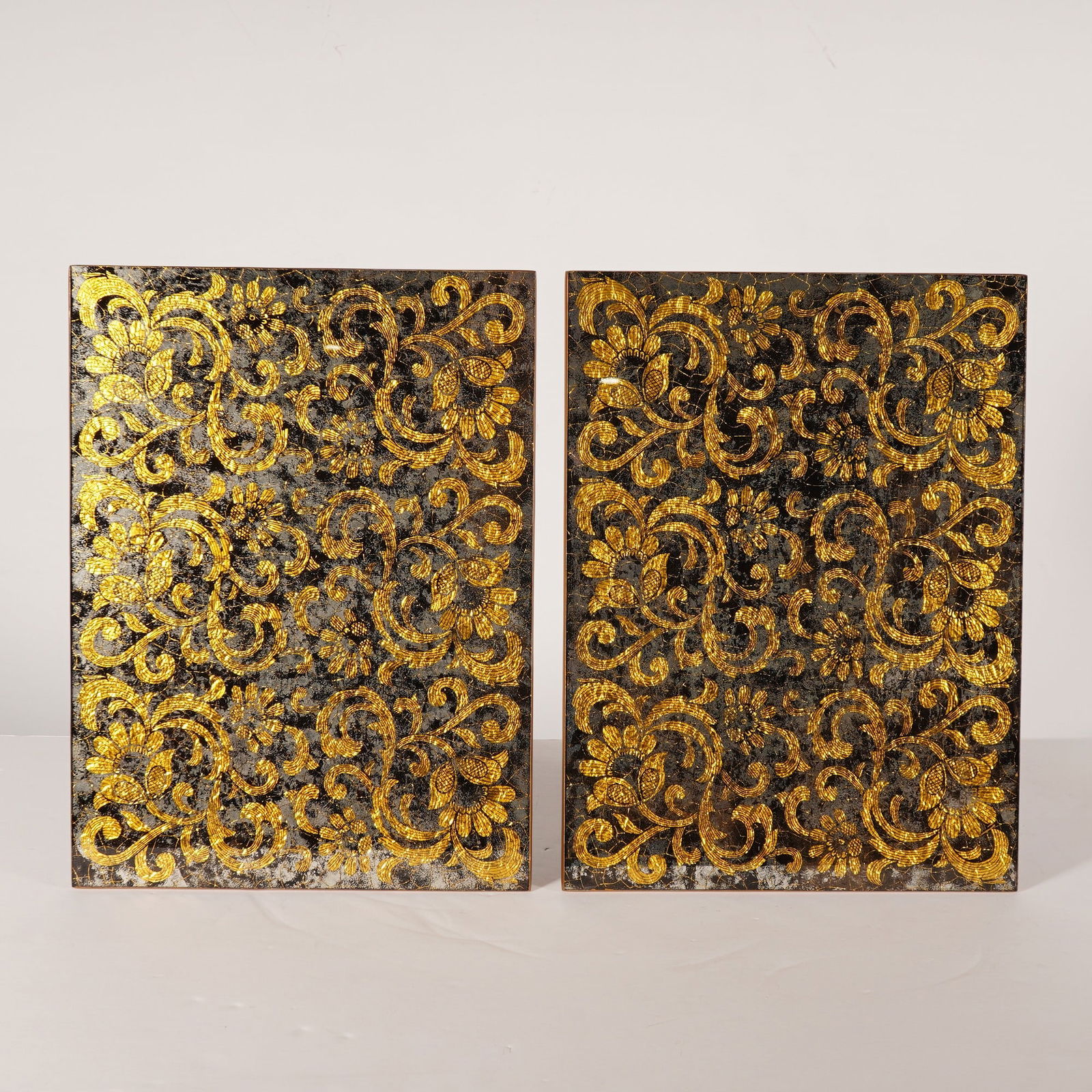 2pc Nomi K Black and Gold Glass Lace Motif Mirror Placemats: A pair of rectangular glass placemats by Nomi K featuring a lace motif. Each piece is constructed with a mirrored glass surface decorated with an all-over scrolling floral and foliate pattern in textu