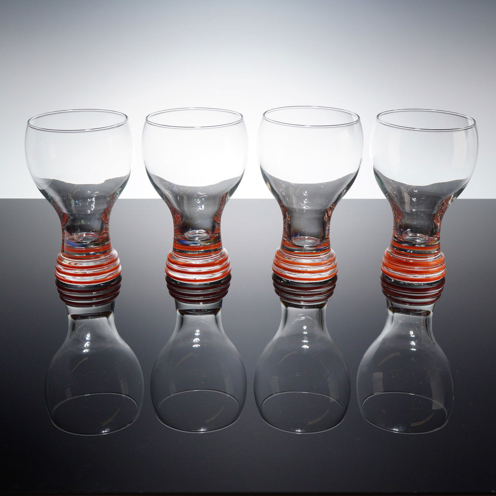 4pc Homer Laughlin Fiesta Ware Banded Water Goblets: A set of Homer Laughlin Fiesta ware water goblets featuring clear glass bowls that taper into weighted solid glass bases. Each vessel is decorated with three horizontal concentric bands in the Persimm