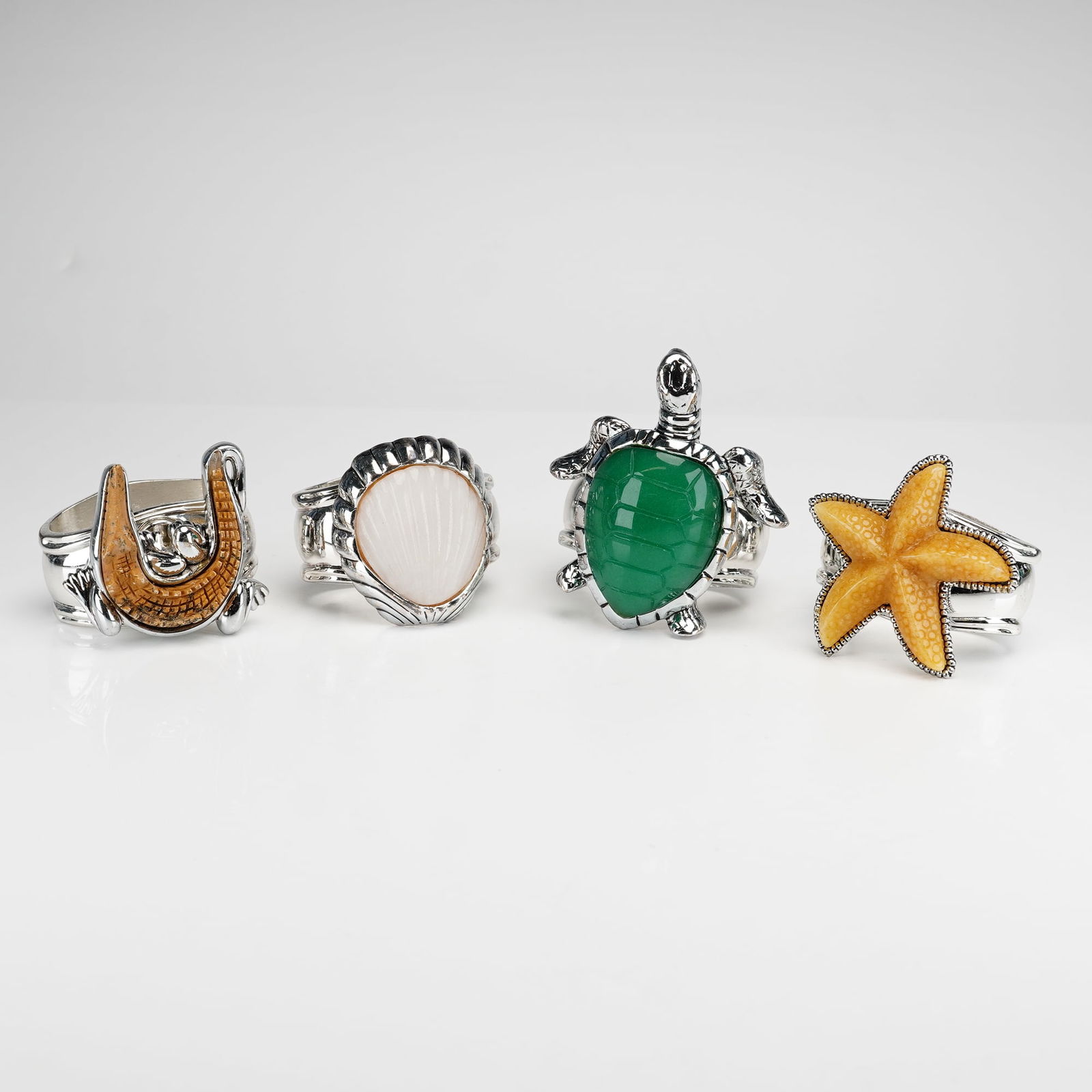 4pc Hans Turnwald Silverplated Napkin Rings: A set of 4 Hans Turnwald silverplated napkin rings featuring nature-inspired motifs. The collection includes a turtle, starfish, shell, and alligator. Each piece is constructed with a wide, polished b