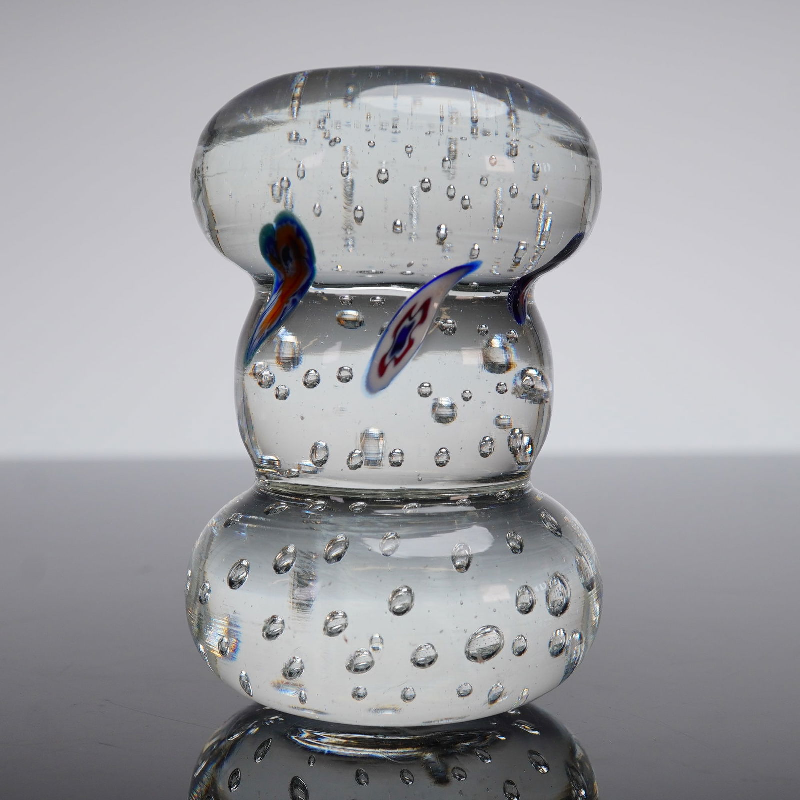 Contemporary Art Glass Studio Paperweight: The item features a distinctive hourglass silhouette composed of three stacked, rounded segments. The glass exhibits numerous controlled air bubbles trapped throughout the form. Embedded within the cl