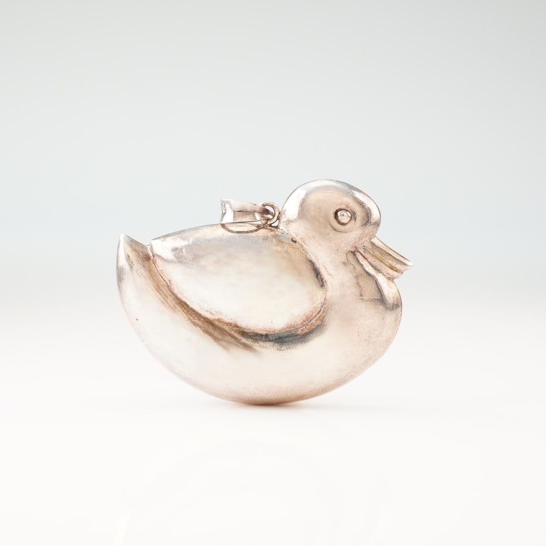 Sterling Silver Stylized Duck Pendant: This pendant is crafted from sterling silver and designed in the form of a stylized duck. The piece features a puffed construction with a polished finish. The pendant is fitted with a simple tapered b