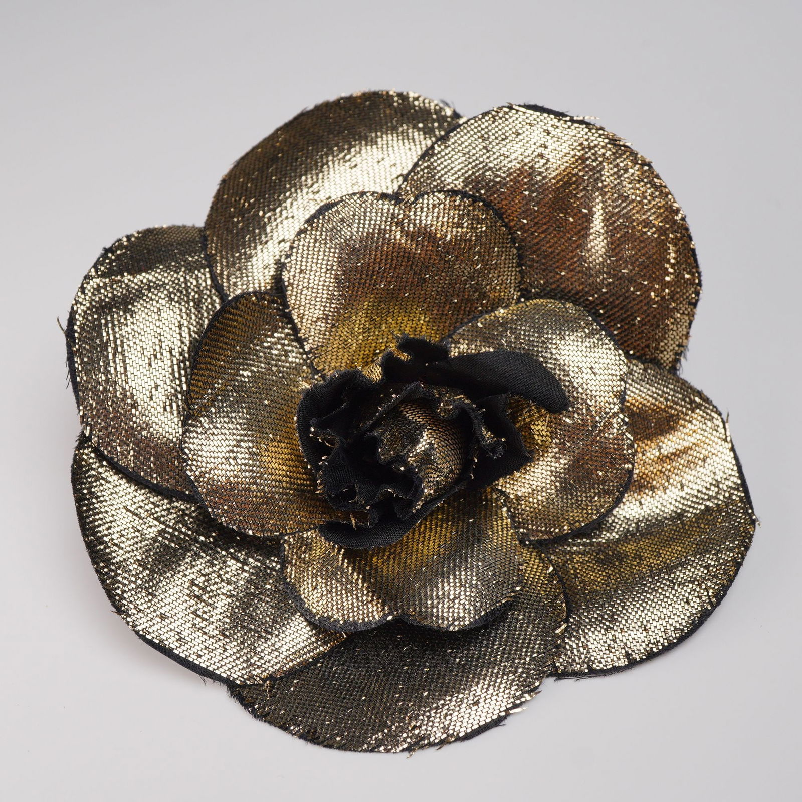 Chanel Paris Metallic Gold and Black Camellia Fabric Brooch: A Chanel camellia fabric brooch constructed from layered petals of metallic gold and black woven textile, providing a shimmering, textured appearance, centered by gathered black fabric. The reverse si