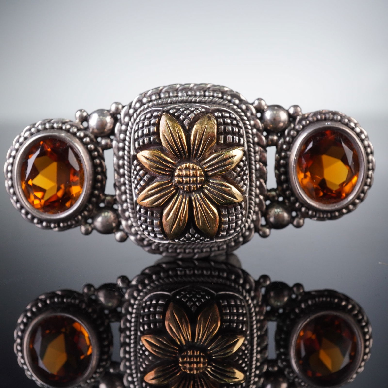 Stephen Dweck Sterling Silver and 18K Gold Accent Citrine Brooch: A substantial and highly textural brooch by designer Stephen Dweck, crafted in oxidized sterling silver. The piece features a central rectangular plaque accented with a raised eight-petal flower in 18