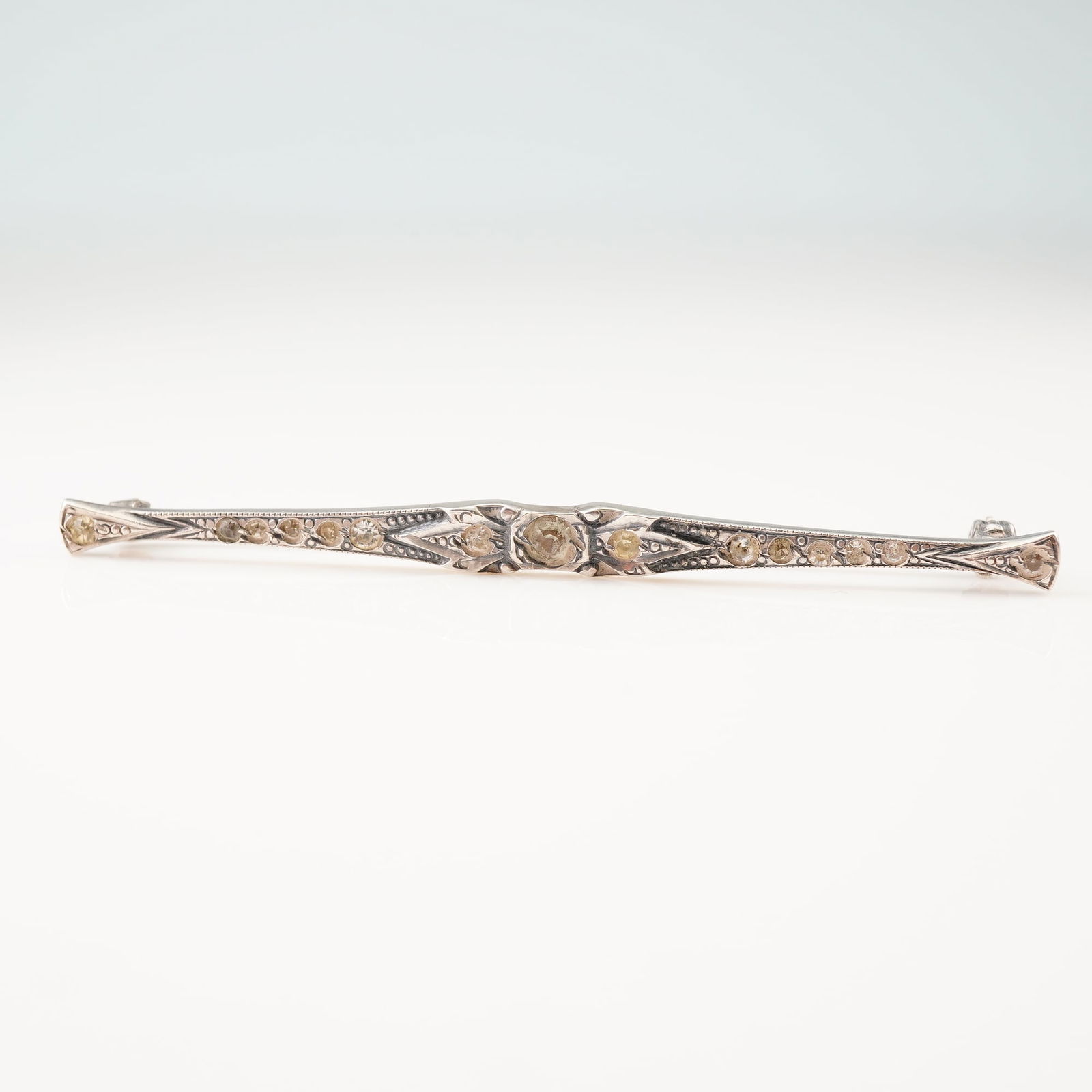 Sterling Silver Art Deco Style Bar Brooch: This Art Deco style bar brooch is crafted from sterling silver and features a long, slender, tapered bar design. The piece is decorated with geometric milgrain detailing and a central circular focal