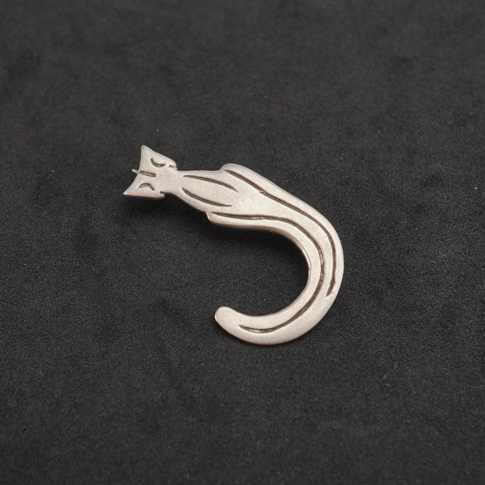 Sterling Silver Stylized Cat Brooch Pin: A sterling silver brooch crafted in a stylized Modernist design. The piece depicts an elongated cat figure with an arching body and tail, rendered in smooth, polished silver with incised lines