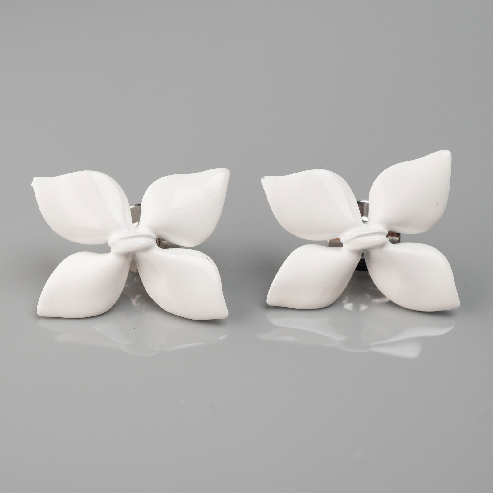 A Pair of Christian Dior White Enamel Flower Earrings: A pair of Christian Dior earrings, each designed as a stylized four-petal flower. The pieces are crafted from white enameled metal or durable resin. The reverse of each flower is affixed with a