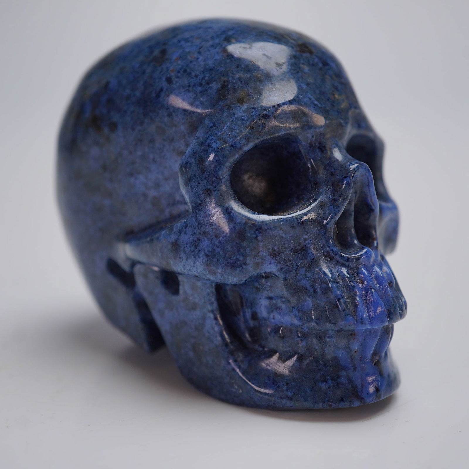 Sodalite Crystal Hand-Carved Skull Sculpture: A modern decorative sculpture of a human skull, hand-carved from polished natural sodalite. The stone exhibits a deep cobalt blue color heavily mottled with black, grayish, and lighter blue mineral in