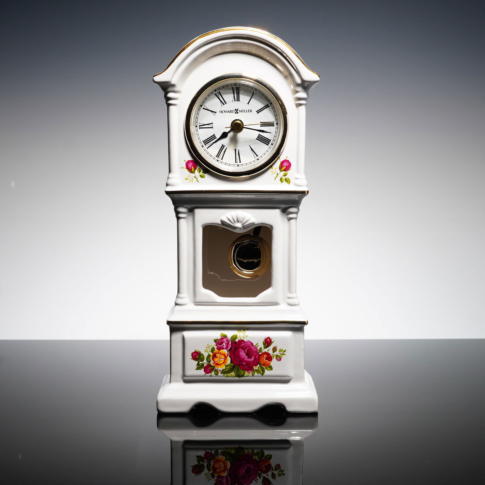 Howard Miller Porcelain Grandmother Mantel Clock: A Howard Miller porcelain grandmother mantel clock featuring a floral rose design. The piece is constructed from white glazed ceramic with gold-toned accents along the edges. The clock face displays b