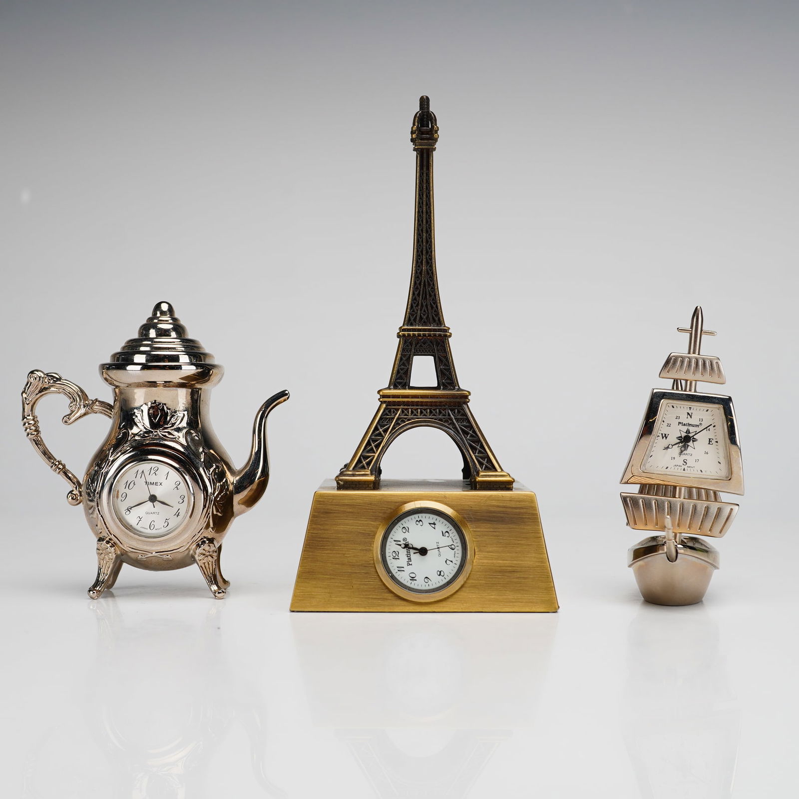3pc Miniature Clocks by Timex and Platinum: The collection of vintage miniature desk clocks featuring quartz movements integrated into decorative metal forms. The collection includes an ornate silver-toned teapot with a Timex branded clock face