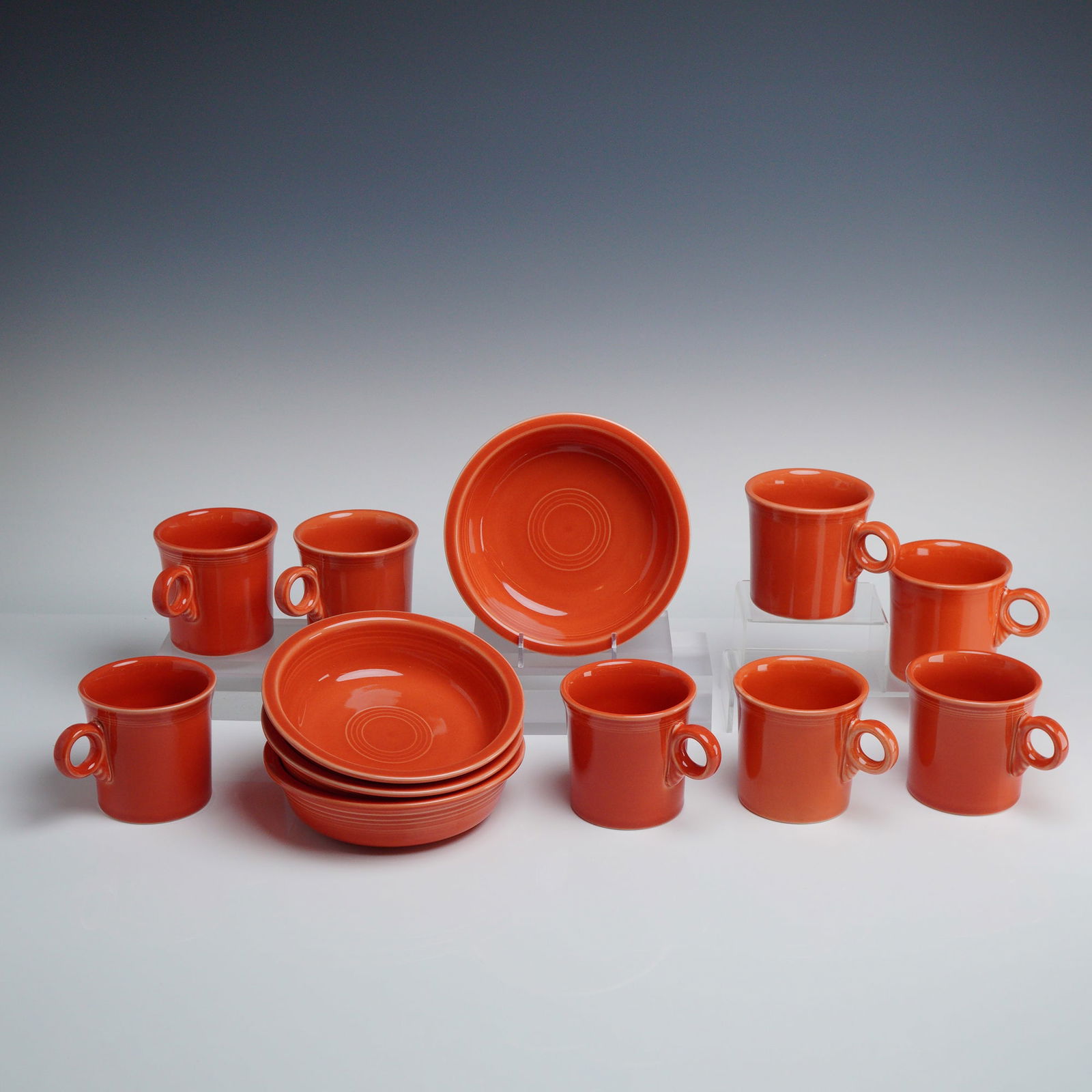 Set of 12 Homer Laughlin Fiesta Ware Bowls and Mugs: Set includes 4 - 7" bowls and 8 mugs, finished in a uniform Paprika orange glaze. Each piece is constructed of glazed ceramic and features the signature concentric ring design characteristic of the Fi
