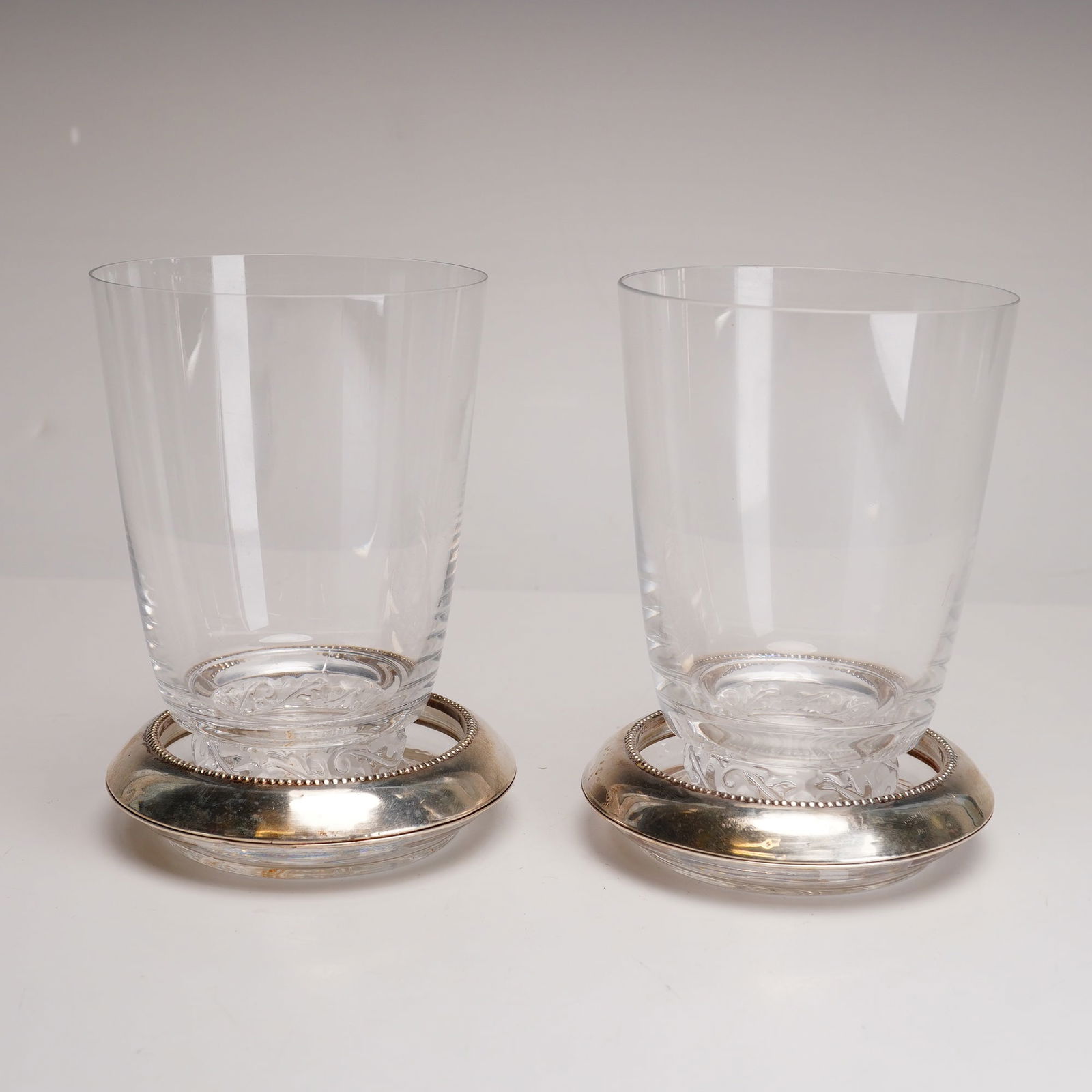 4pc Lalique and Frank M. Whiting & Co. Tumblers and Coasters: This 4pc drink grouping including two Lalique Saint Hubert crystal tumblers and two sterling silver and glass coasters from Frank Whiting & Co. is designed in a traditional classical style. The