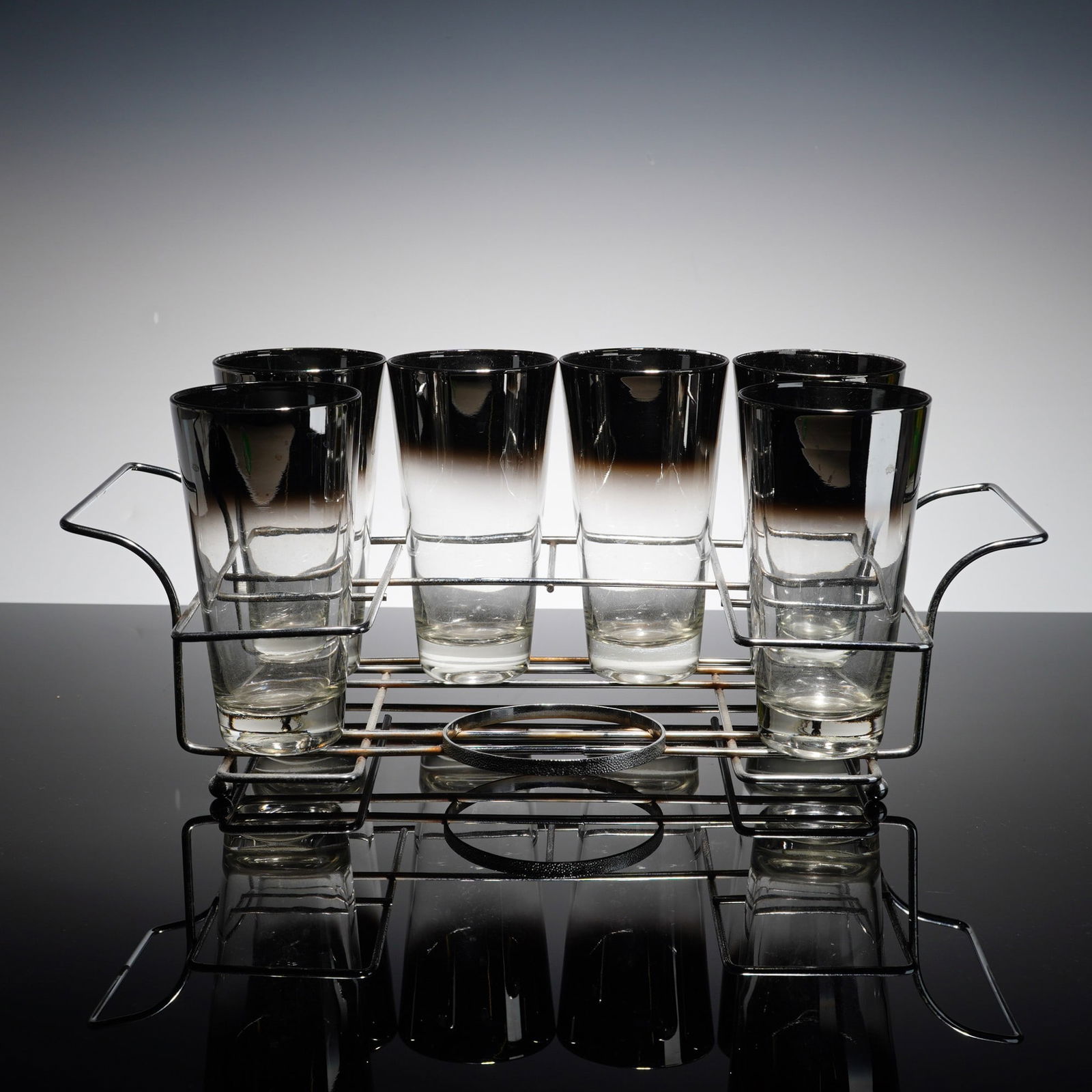 7pc MCM Silver-Plated Rim Tumblers with Rack: The six tumblers feature the signature silver fade design, characterized by a wide metallic silver-toned band at the rim that transitions into clear glass. The accompanying caddy is crafted from
