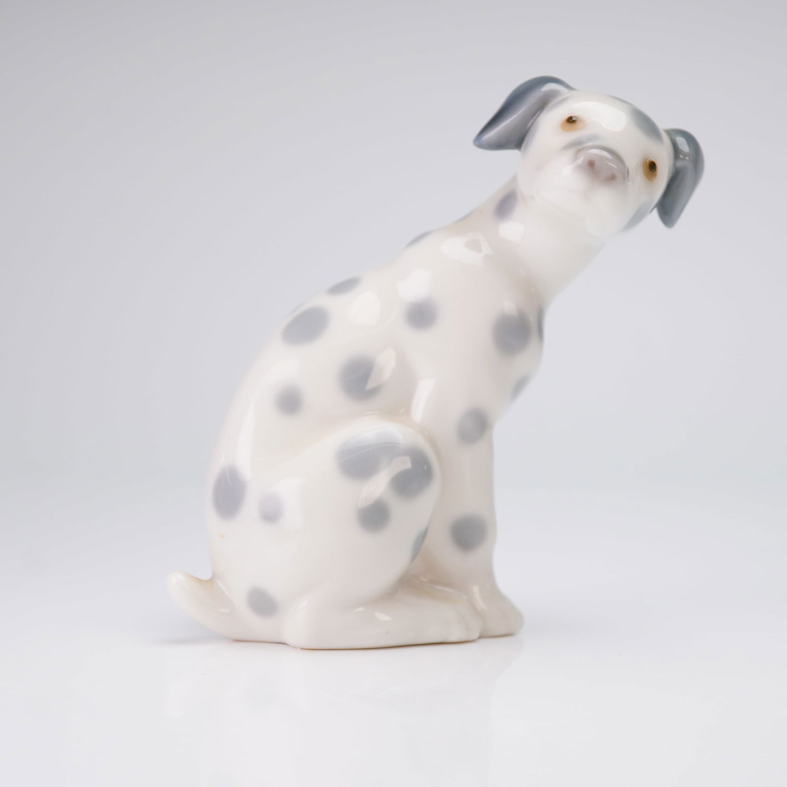 Lladro Porcelain Figurine, Dalmatian 1001260: A glazed porcelain figurine by Lladro, titled "Dalmatian" model 1001260. This figurine depicts a seated puppy rendered in high-gloss white porcelain. The decoration utilizes gray underglaze for the sp