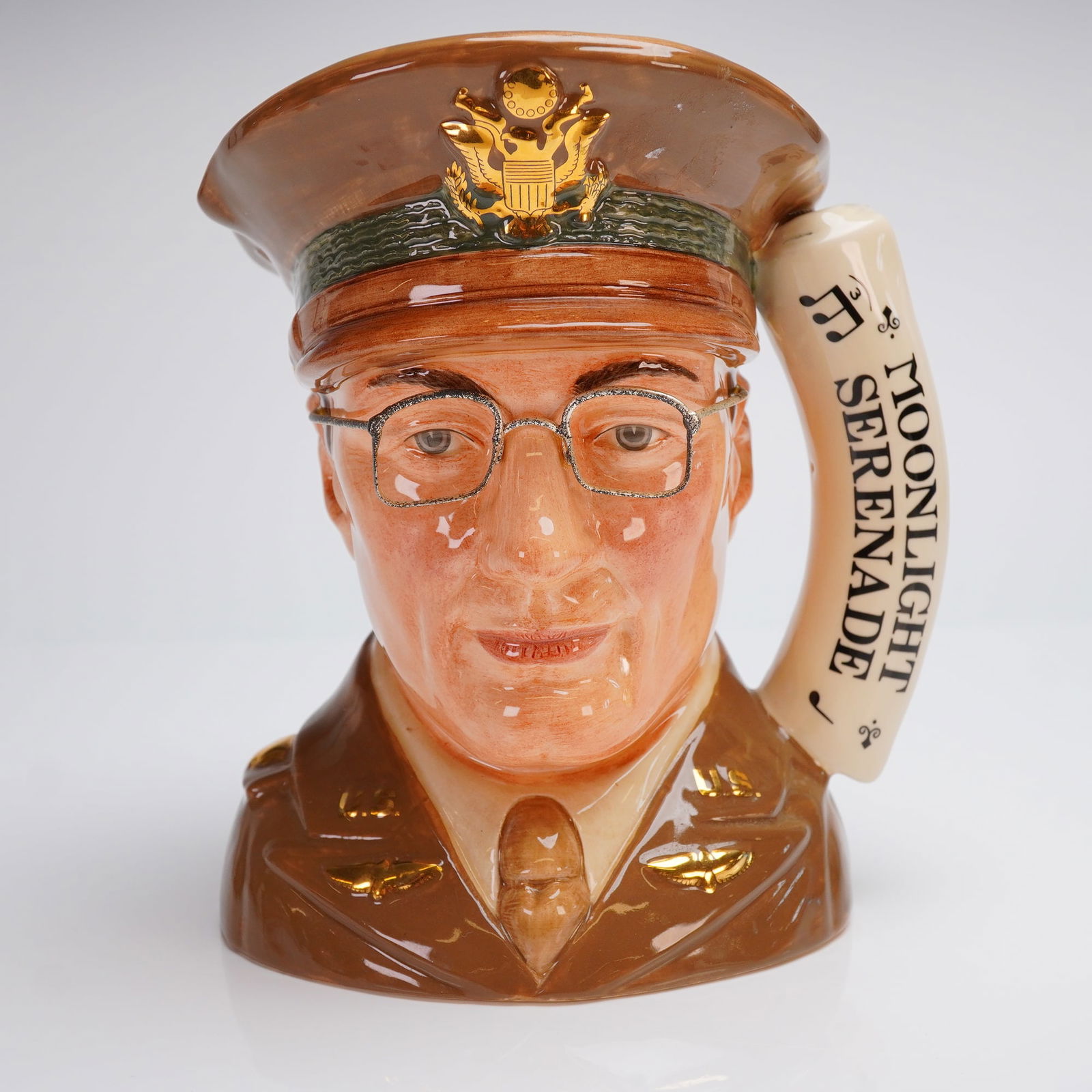 Royal Doulton Large Character Jug, Glenn Miller D6970: The character jug depicts the musician and bandleader Glenn Miller. The jug is executed in a high-gloss multi-color glaze, modeling Miller in a brown military uniform and peaked cap bearing a gold-ton