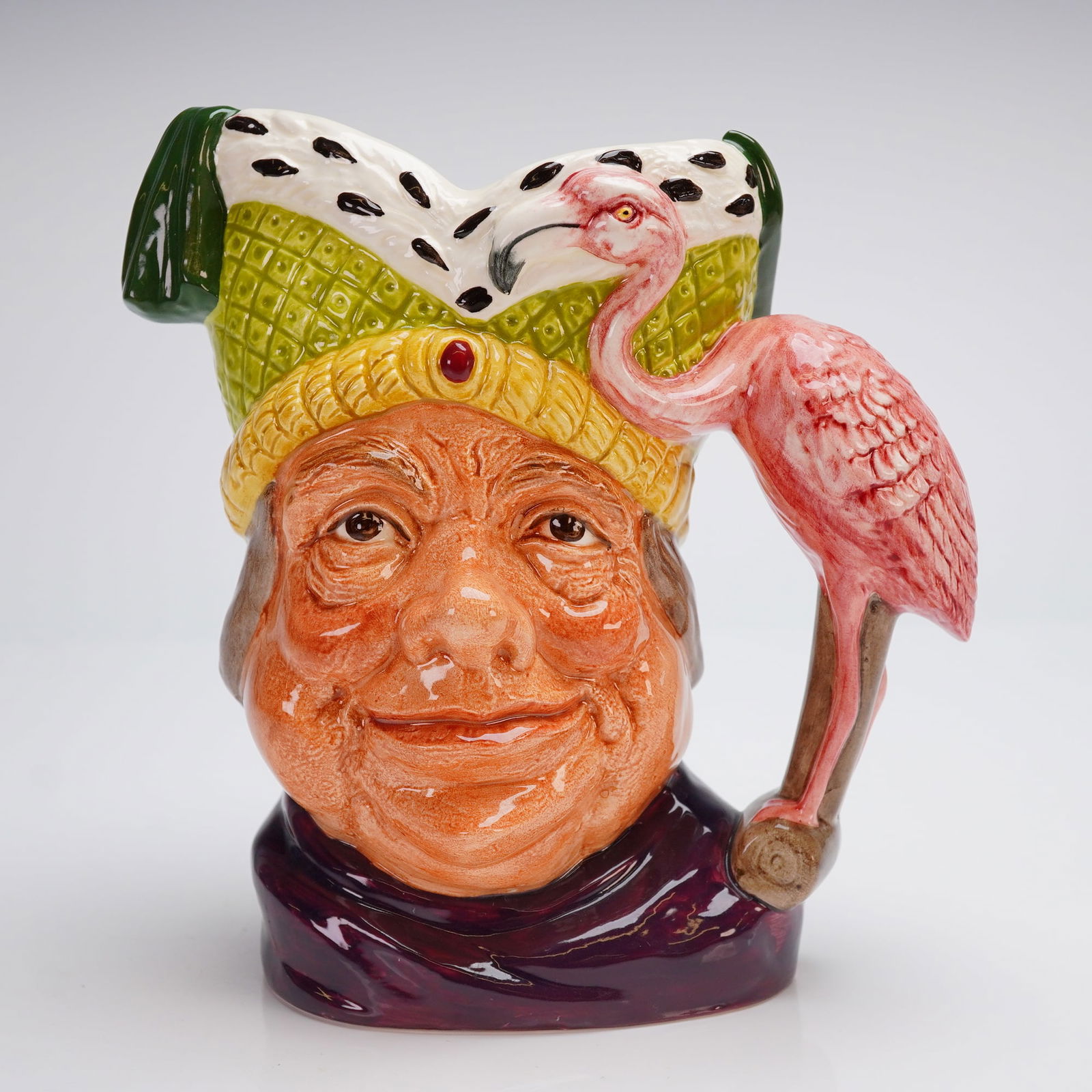 Royal Doulton Large Character Jug, Ugly Duchess D6599: The jug is glazed and depicts the head of the grotesque character wearing a vibrant green and yellow quilted cap, which is adorned with an ermine-spot pattern. The handle is formed by a protruding pin