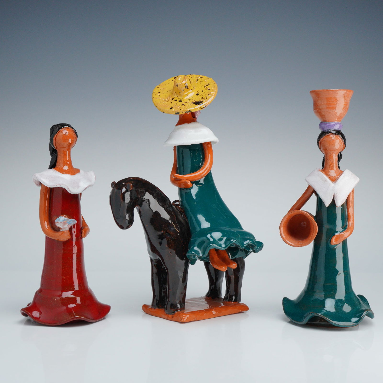 3pc Faceless Folk Art Terracotta Female Figurines: This 3pc terracotta figurines set is composed of hand-modeled clay with a high-gloss glaze. The group includes a standing figure in a red dress holding a bird, a figure in a green dress mounted on a d