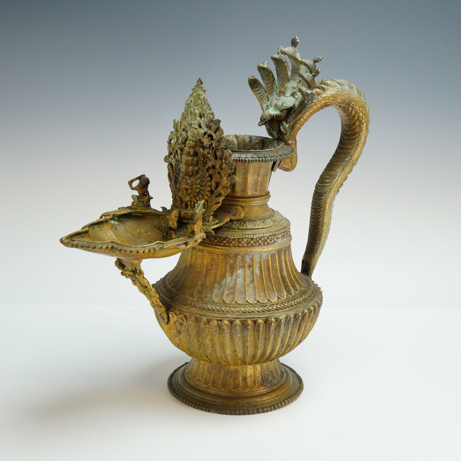 Nepalese Brass Sukunda Ritual Oil Lamp: This antique Nepalese brass ritual oil lamp, known as a Sukunda, is a cast metal vessel featuring a bulbous, gadrooned body set upon a flared, circular footed base with beaded borders. The piece is ch