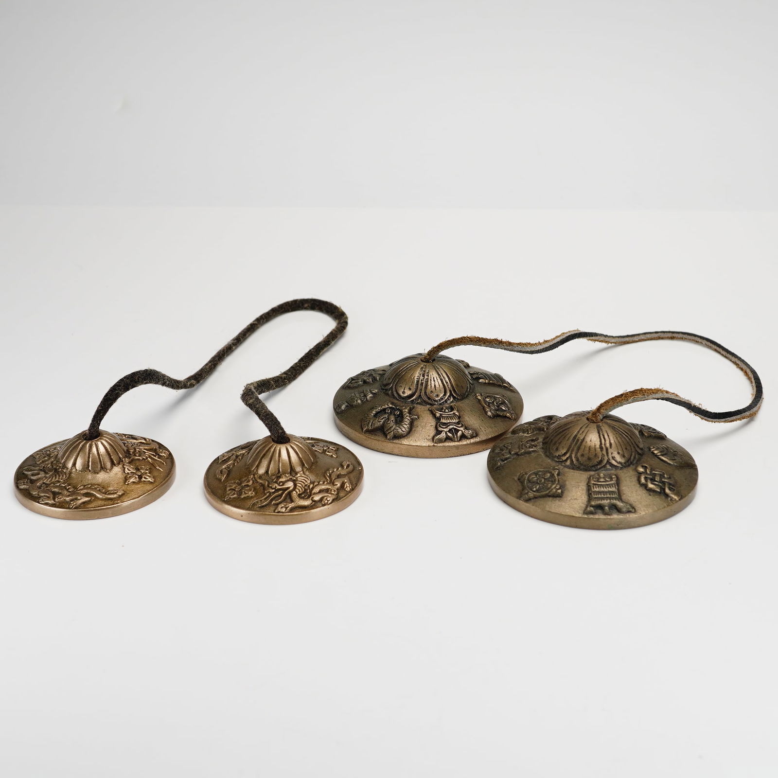 Two Sets of Tibetan Tingsha Cymbals: A collection consisting of two sets of Tibetan Tingsha cymbals cast in metal. The first pair features embossed dragon motifs and double dorje symbols on the exterior surface, centered by a fluted boss