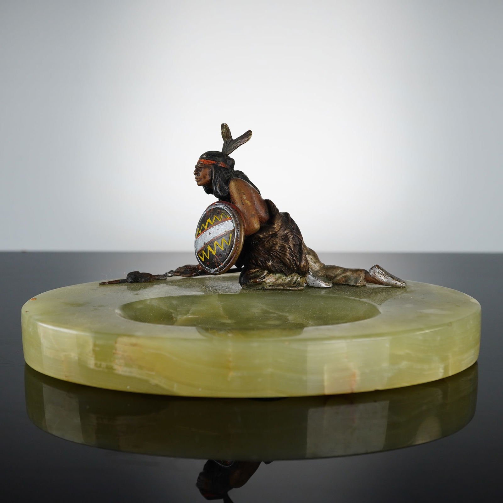 Austrian Onyx Ashtray with Native American Figure: Features a cold-painted spelter figure of a Native American warrior in a dynamic crawling pose. The warrior is depicted holding a decorated shield and a spear, showing vintage details and a multi-colo