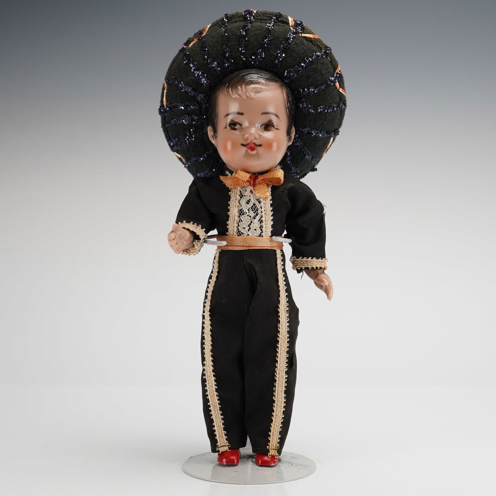Mexican Folk Art Mariachi Doll: The doll features a molded head and body, likely constructed from composition or hard plastic, with hand-painted facial features. The figure is dressed in a traditional black felt or cloth suit, heavi