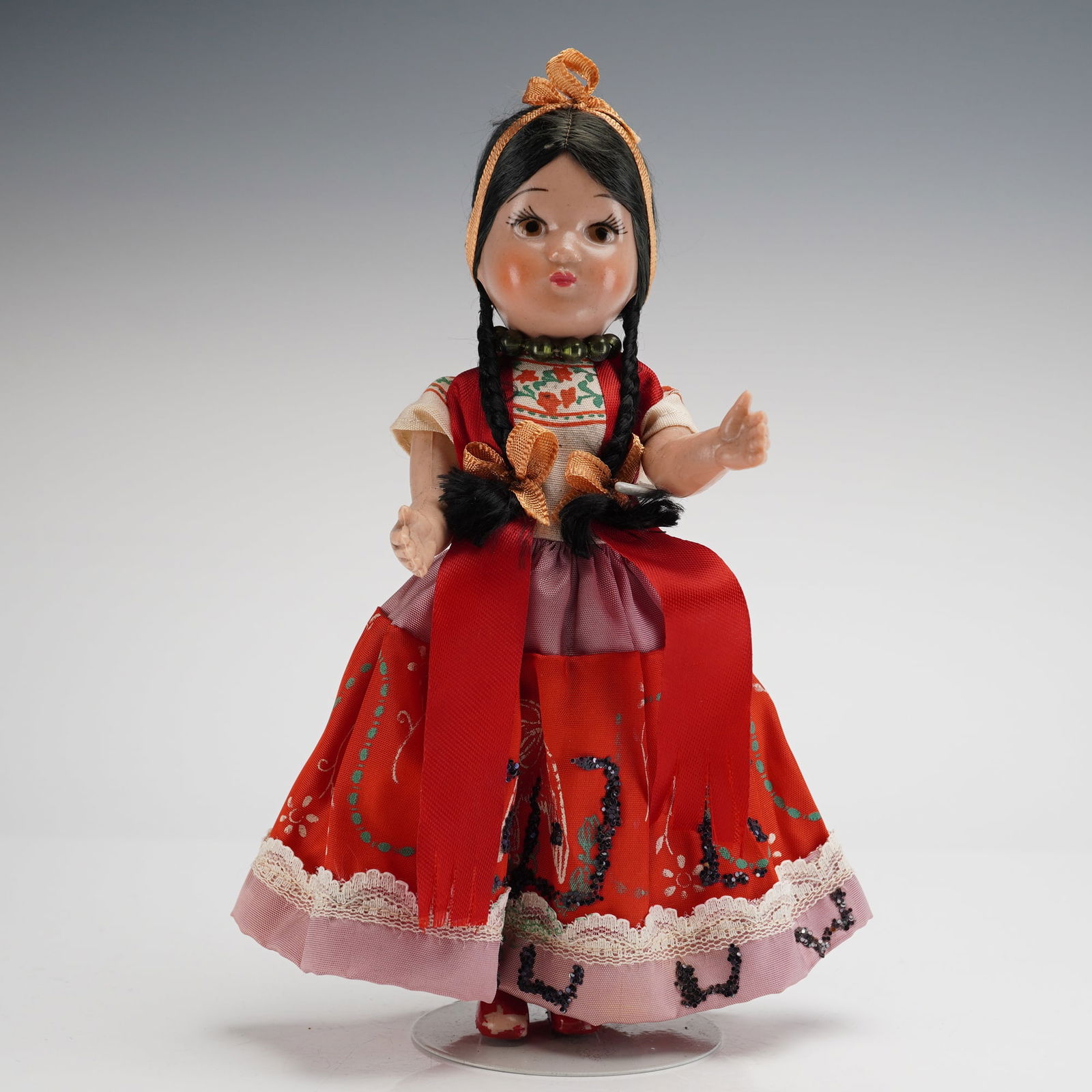 Vintage Mexican Folk Costume Doll: The doll features a molded plastic or composition head and hands with painted facial features and synthetic black braided hair secured by an orange ribbon headband. The attire is a vibrant traditional