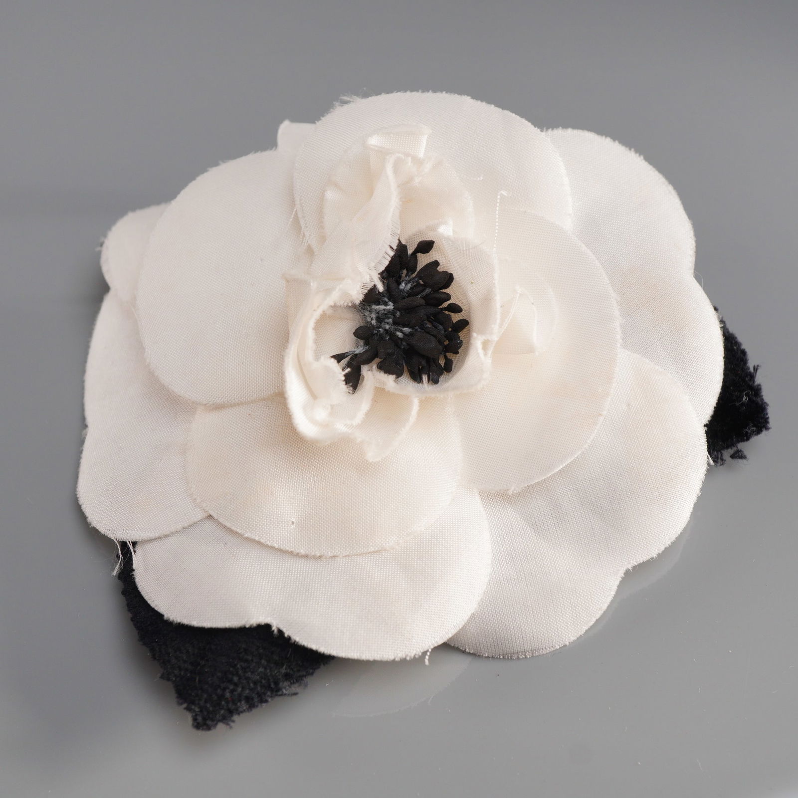 Chanel Paris Black and White Camellia Fabric Brooch Corsage: A Chanel camellia fabric brooch corsage that features layered white textile petals surrounding a textured black fabric center. The reverse of the accessory is fitted with two black fabric leaves and a