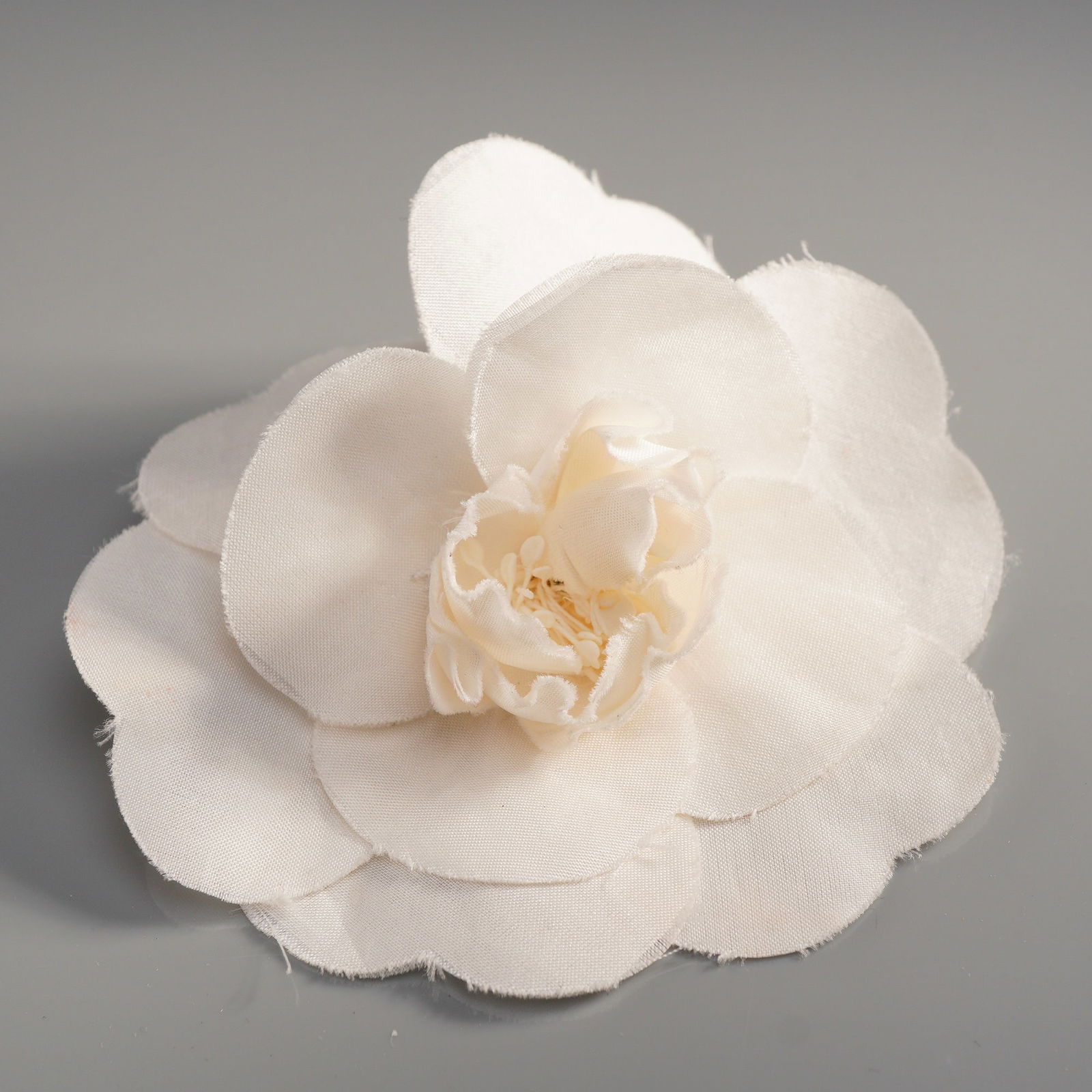 Chanel Paris Camellia White Fabric Brooch: A Chanel camellia fabric brooch, constructed from multiple layers of white fabric, styled as a floral corsage. The edges of the petals are stylized with a slightly unfinished appearance characteristic
