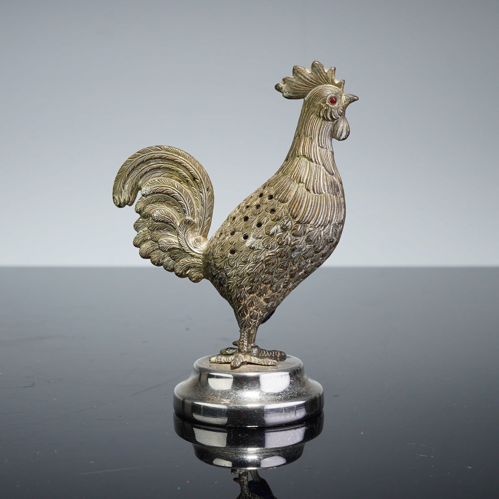 Brass Rooster Pin Cushion: A brass figural rooster pin cushion modeled as a standing bird with realistic plumage. The figure is adorned with red cabochon eyes and features a silver-toned finish. The back is cast with multiple p