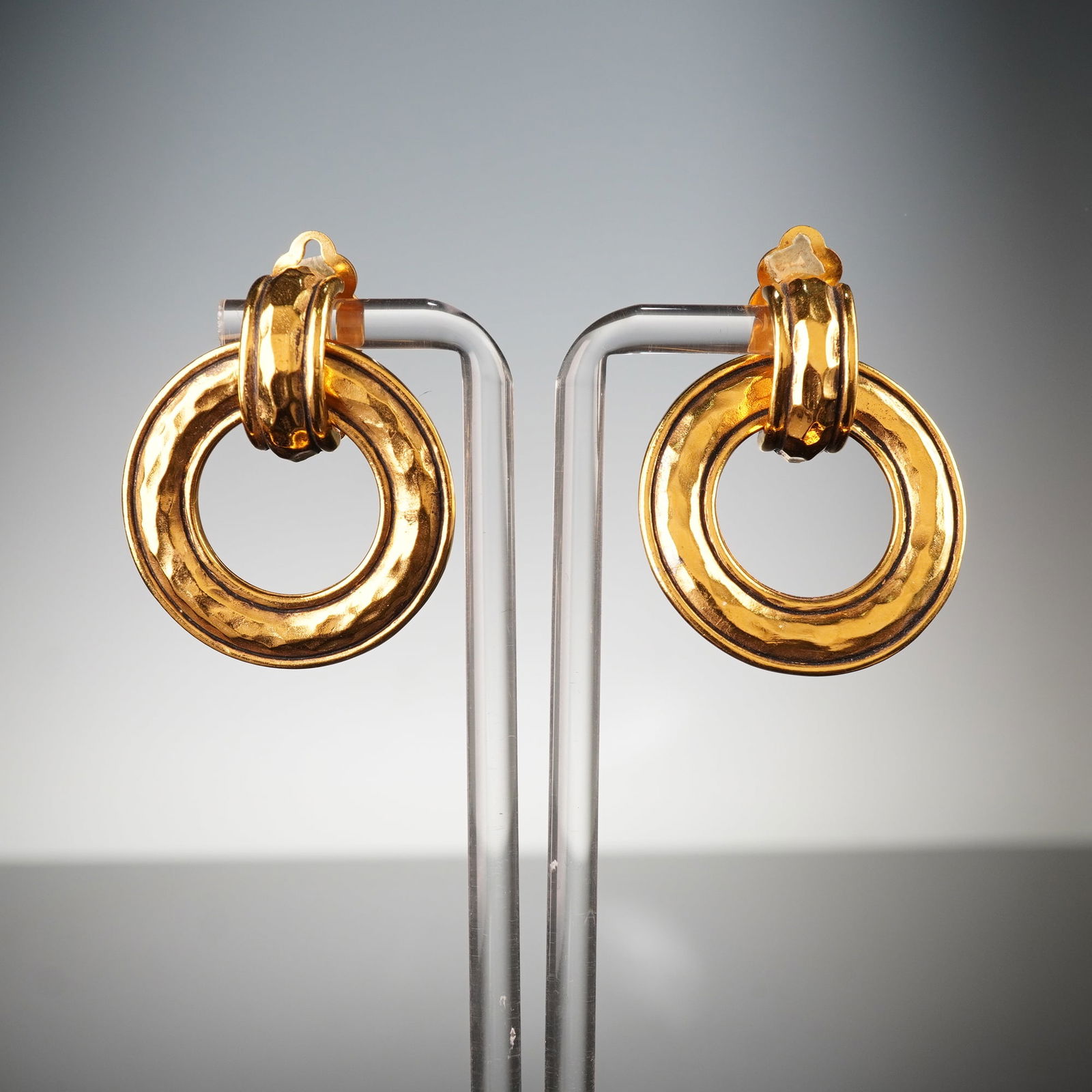 Chanel Gold-Tone Hammered Door Knocker Clip-On Earrings: A pair of Chanel gold-tone hammered door knocker clip-on earrings. Each earring features a U-shaped top element that suspends a substantial, open circular drop. Both components display a distinctive h