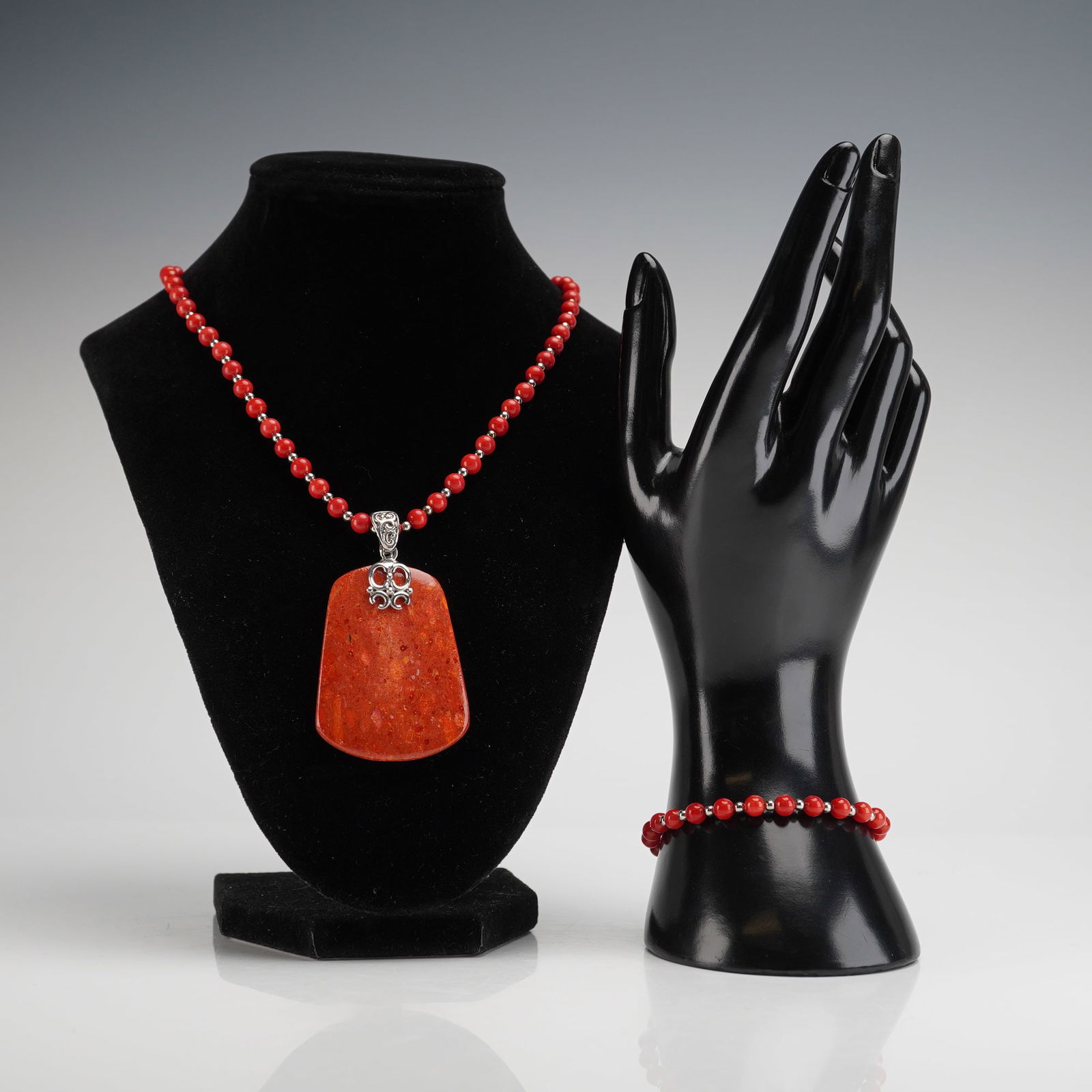 BBJ Sterling Silver and Red Coral Bead Pendant Necklace and Bracelet: A beaded bracelet and necklace set featuring red spherical coral beads interspersed with small sterling silver spacer beads. The necklace is accented with a large, flat trapezoidal coral pendant suspe