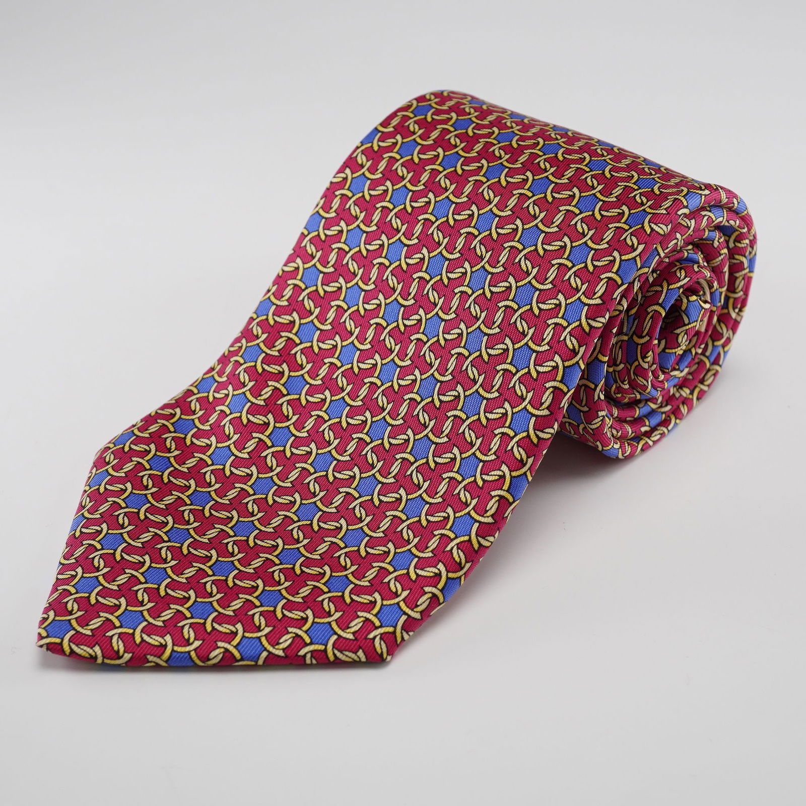 HERMES PARIS Silk Necktie, Red with Gold Interlocking Rings and Blue Star: A HERMoˆS PARIS silk necktie, featuring a vibrant red ground with a repeating geometric pattern of interlocking gold-toned rings or chain links, interspersed with small blue star-like motifs. The rev