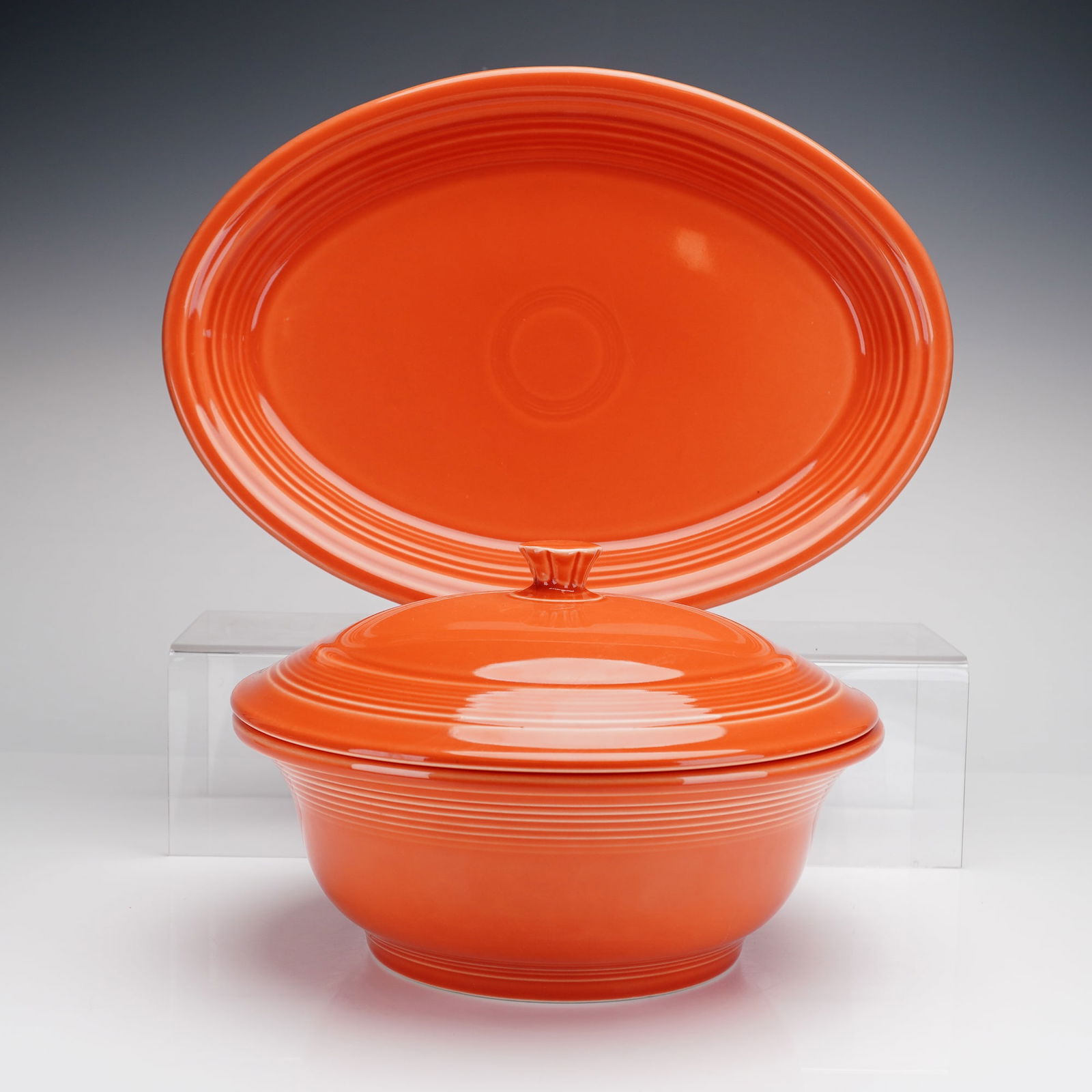 2pc Set of Homer Laughlin Fiesta Ware Covered Serving Bowl & Oval Platter: A 2pc Homer Laughlin Fiesta ware set of covered serving bowl and oval platter. Each ceramic piece is finished in a high-gloss orange glaze and features the brand's signature Art Deco-inspired concentr