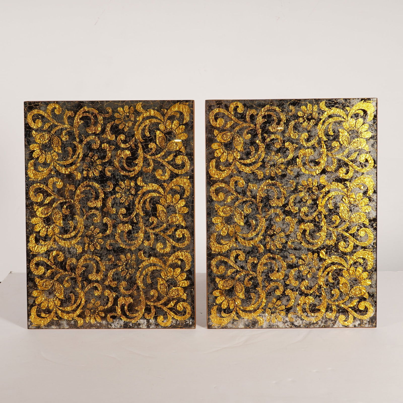 2pc Nomi K Black and Gold Glass Lace Motif Mirror Placemats: A pair of contemporary rectangular glass mirror placemats by Nomi K featuring a black and gold lace motif. Each piece is decorated with an intricate floral and scroll design executed with gold leaf de