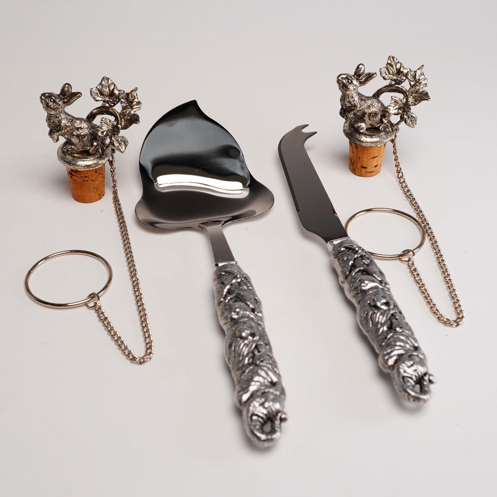 Arthur Court Serving Utensils and Bottle Stoppers: Two sets of Arthur Court serving utensils including a cheese slicer and serving set and figural cork bottle stoppers. These contemporary animalier style pieces are crafted with sand-cast aluminum hand
