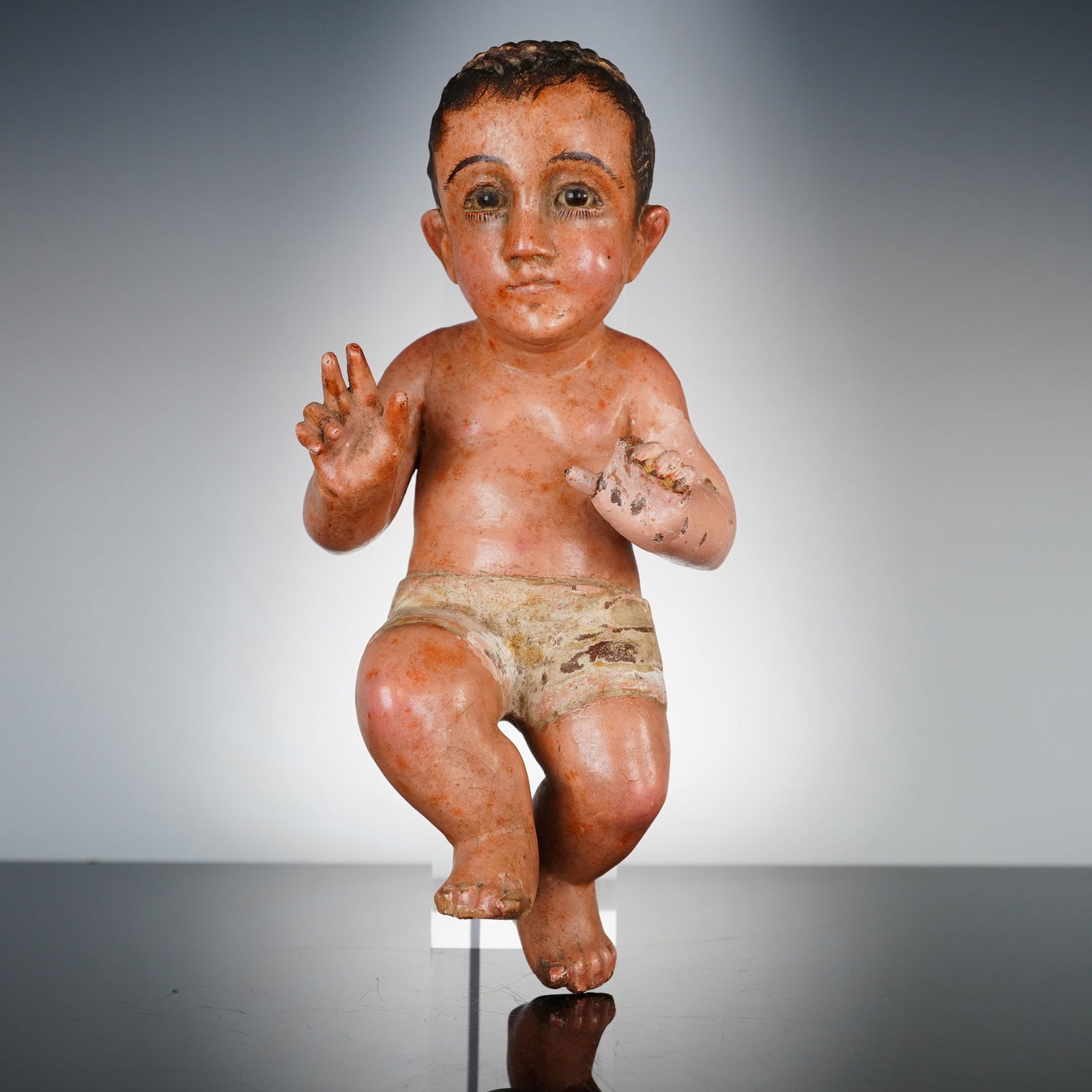 Spanish School 18th Century Polychrome Wood Nino Jesus: This 18th century Spanish polychrome wood sculpture depicts the Christ Child, painted in tempera. The figure is rendered as an infant with inset glass eyes and textured dark hair, posed with the right