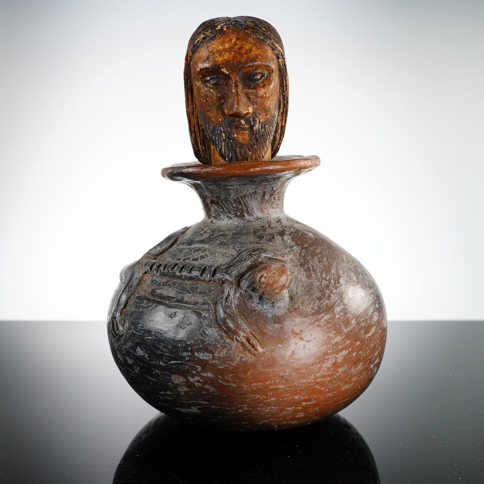Latin American Figural Vessel with Religious Carved Head Stopper: This lot features a late 20th-century Latin American figural vessel of ceramic construction paired with a hand-carved wooden stopper. The ceramic vessel is globular in form with a flared rim and is fi