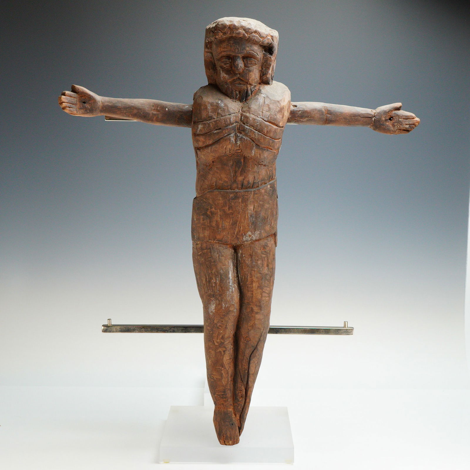 Spanish Colonial Carved Wooden Corpus of Christ: This Spanish Colonial carved wooden corpus of Christ is executed in a primitive folk-art style. The figure is hand-carved from a dark wood and features a crown of thorns, a beard, and stylized anatomi