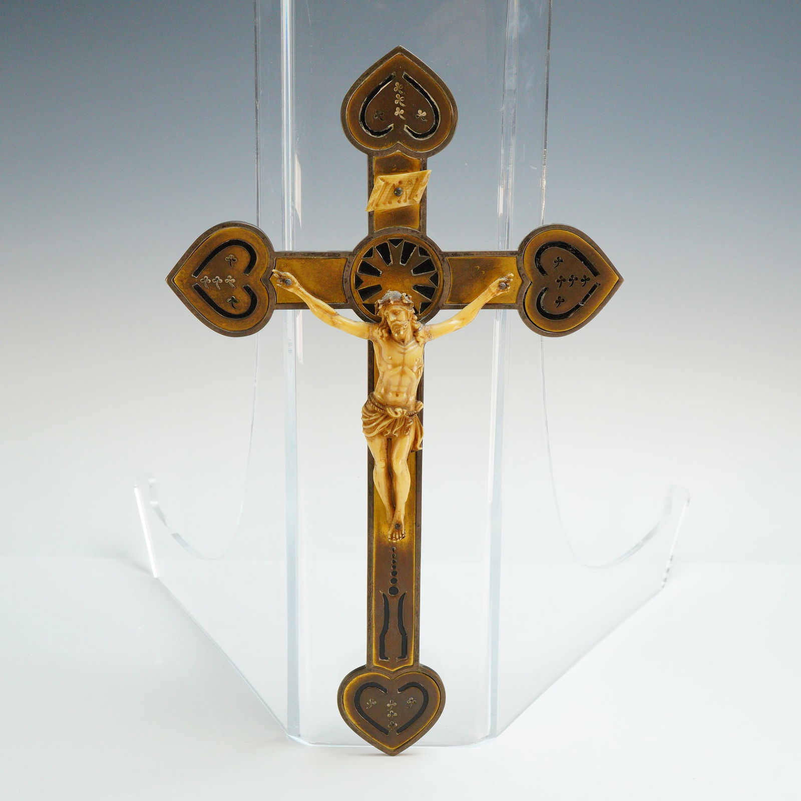 Metal Crucifix with Carved Corpus and Champleve Enamel: This antique metal crucifix features a carved corpus, mounted to a decorative metal cross. The cross is constructed from a yellow-toned metal, such as brass or bronze, and is embellished with champlev