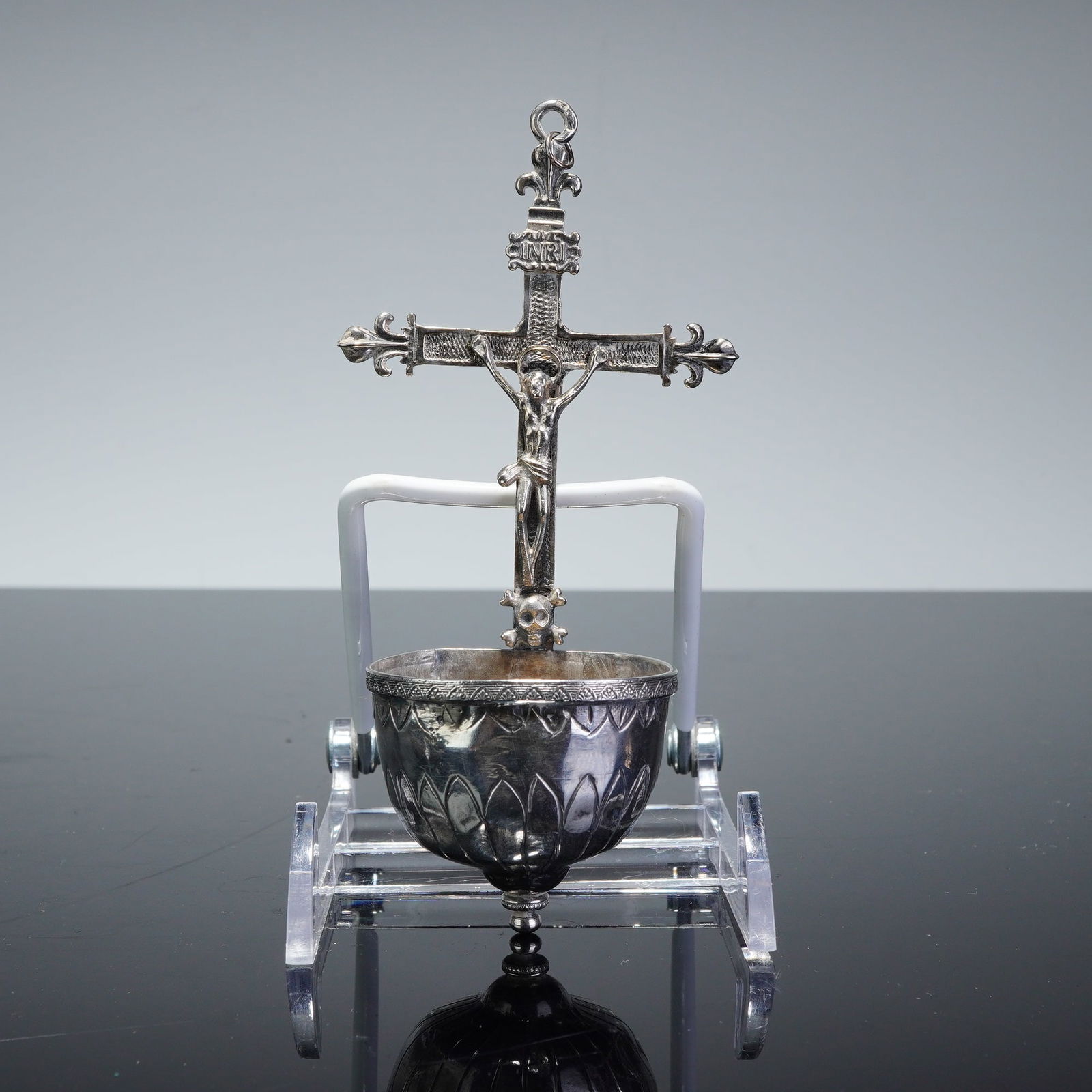 Silver-Toned Metal Jesus on the Cross Holy Water Font: A silver-toned metal hanging holy water font featuring a central crucifix with fleur-de-lis terminals and a corpus Christi. An INRI plaque is positioned above the figure's head, and a memento mori sku