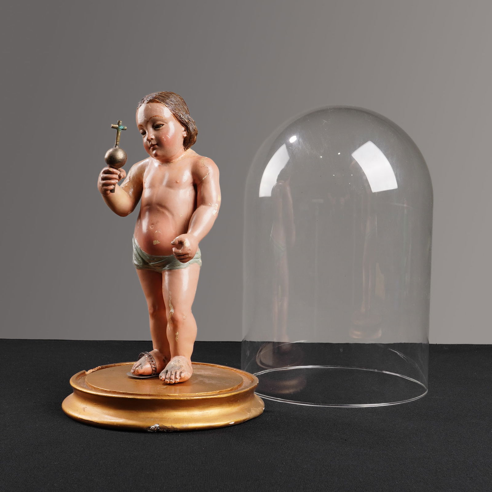 Spanish Santo Christ Child Figure with Glass Cloche: A Spanish polychrome carved wood figure of the Christ Child, mounted on a circular gilded wood base, and covered by a glass cloche. The figure is rendered in an 18th or 19th-century Spanish Colonial s