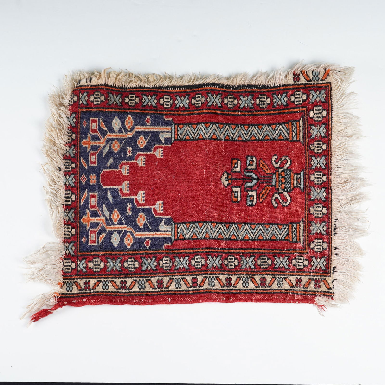 Turkish Handmade Wool Prayer Rug: This handmade wool prayer rug features a traditional mihrab design with a central red field hosting a stylized vase and floral motif. The spandrels are rendered in navy blue with geometric botanical