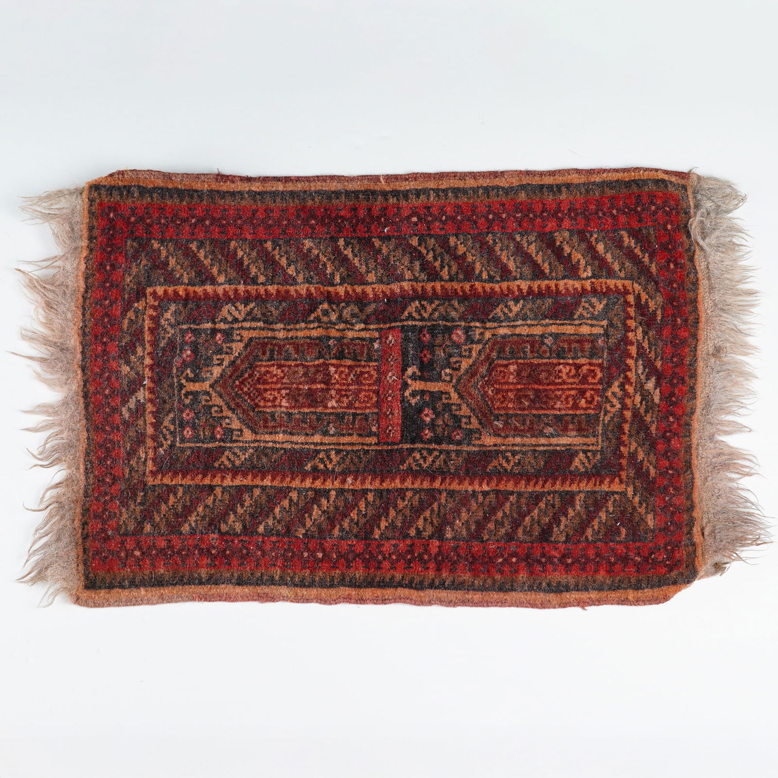 Baluch Afghan Hand-Knotted Prayer Rug: This small hand-knotted rug with fringe ends, featuring a geometric pattern throughout the composition. The textile is constructed with a wool pile on a wool foundation. The central field contains