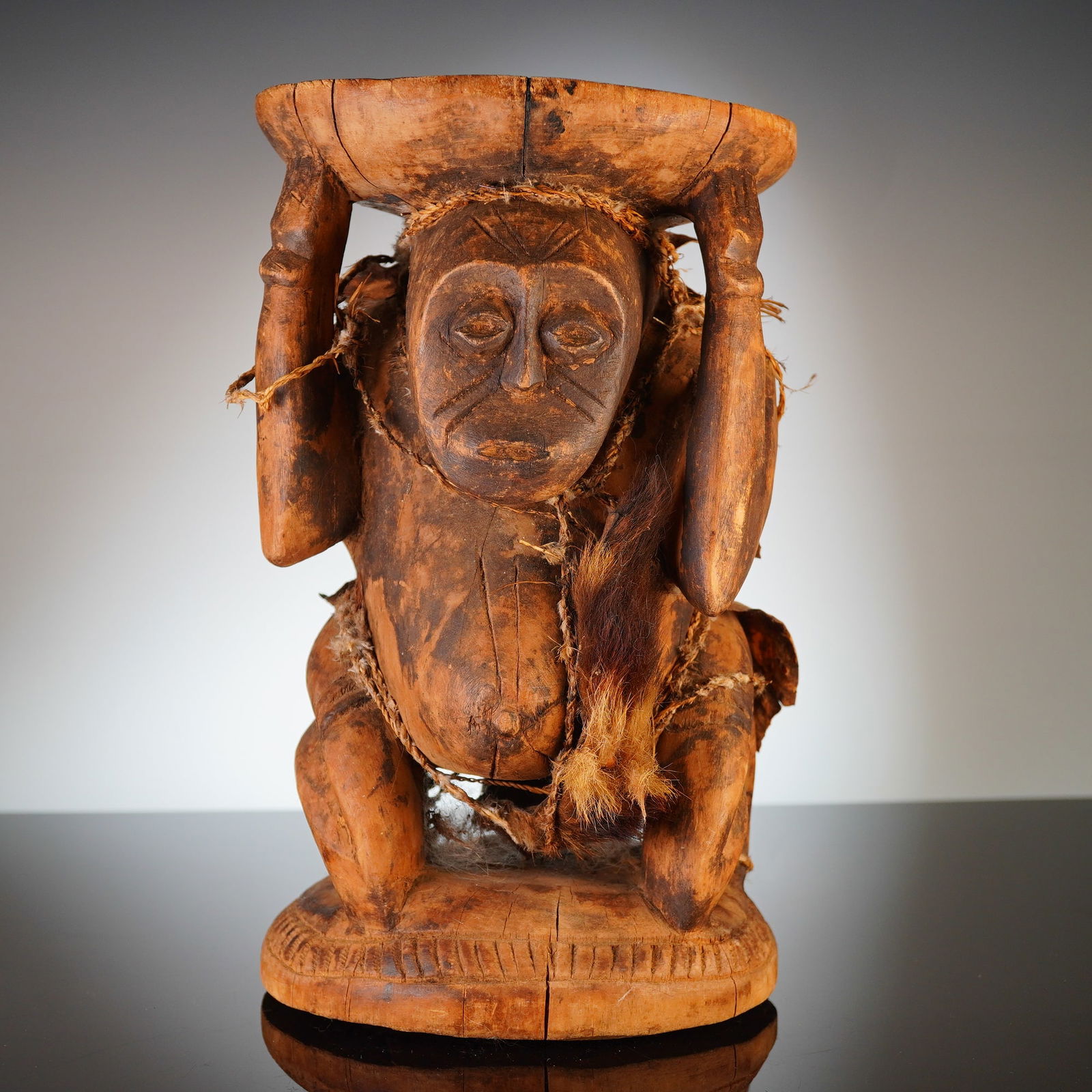 Carved Wooden Ritual Figural Stand: This antique carved wooden ritual figural stand features a bearer figure supporting a tray, carved from a single block of wood. The anthropomorphic figure is depicted in a crouching position with