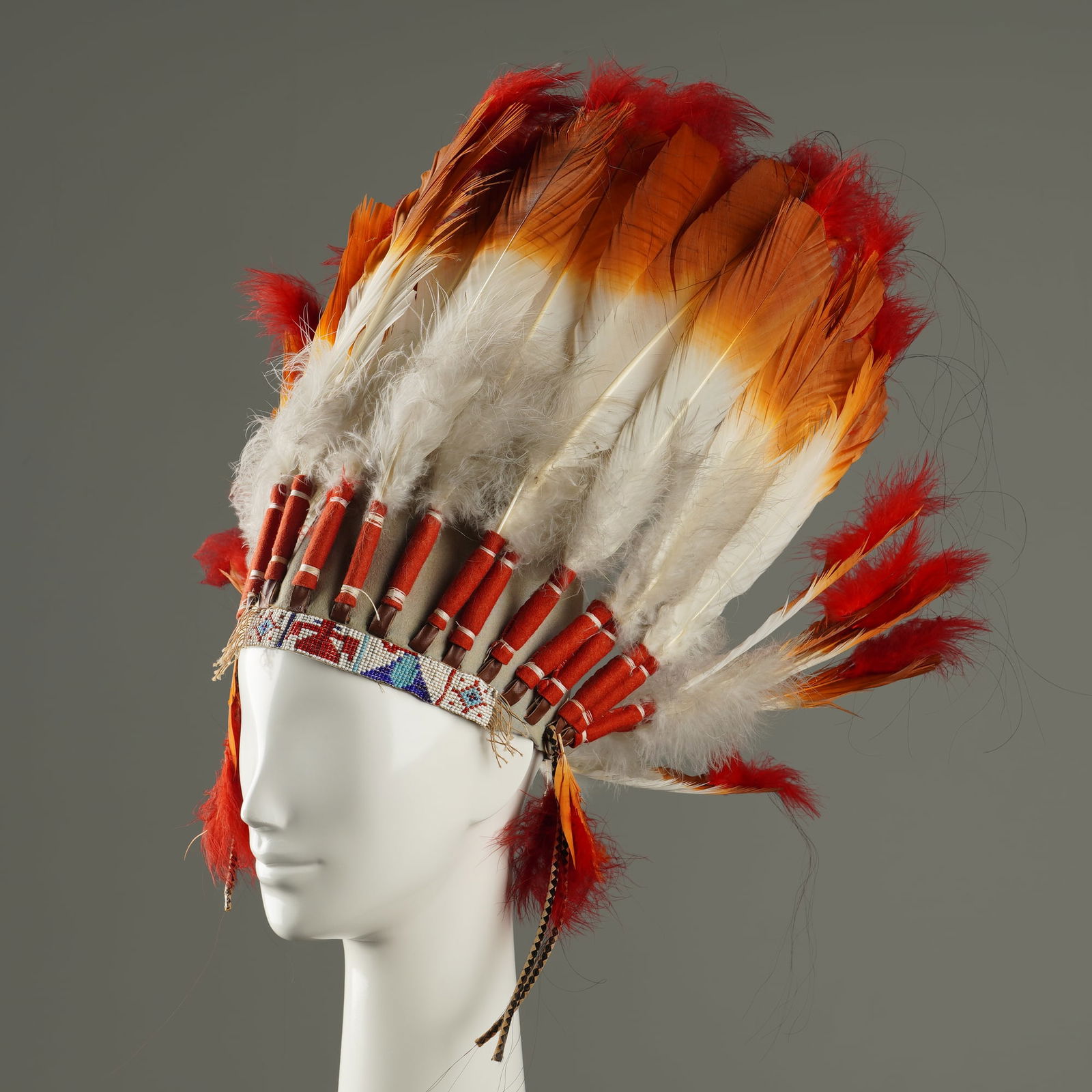 Native American Inspired Feathered Chief Headdress: Native American inspired headdress is constructed on a gray suede-like skullcap. The war bonnet features a flared arrangement of large feathers with white bases, brown vanes, and red downy feather