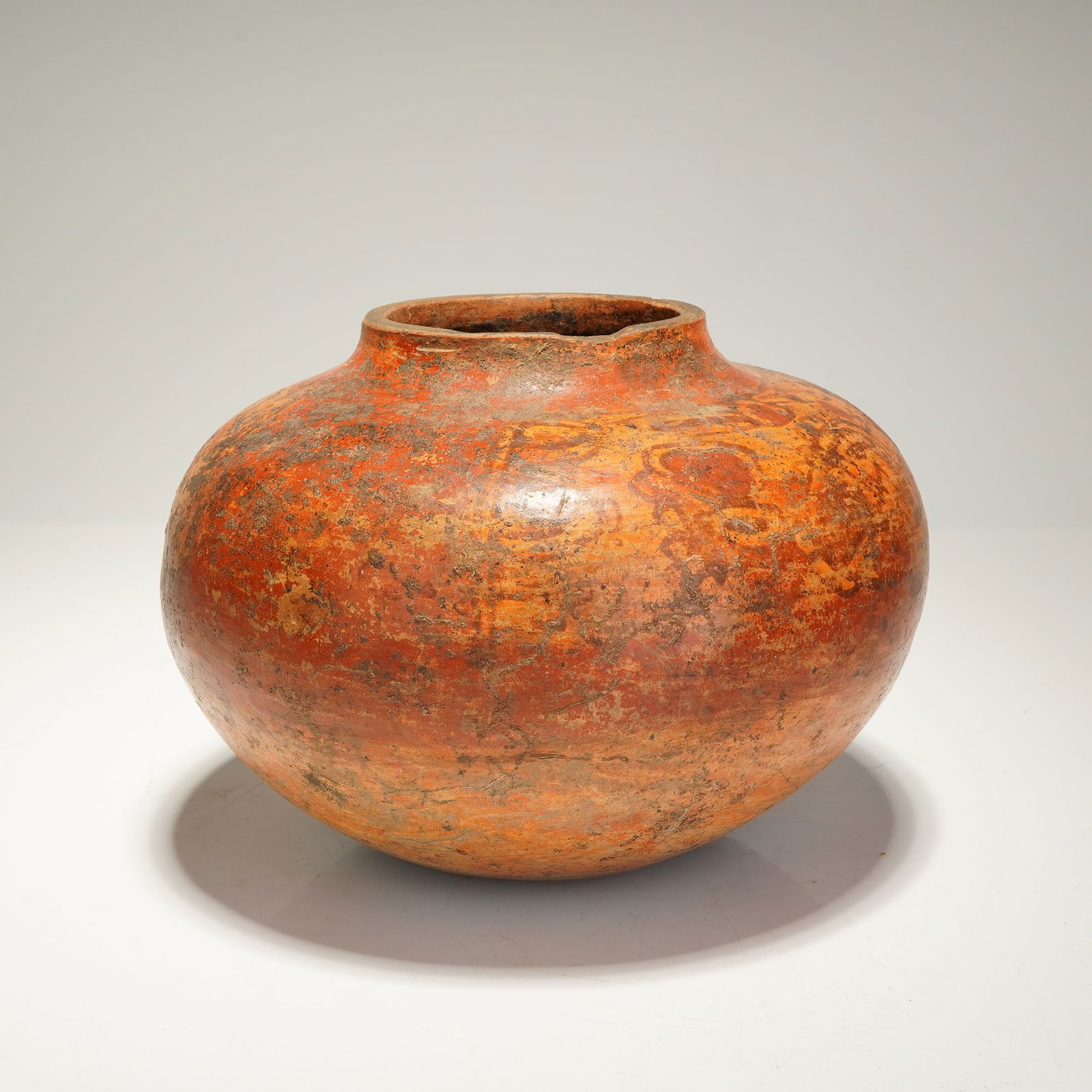 A Pre-Colombian Polychrome Pottery Vessel: This Pre-Colombian polychrome vessel is of squat, globular form, featuring a short, slightly flared neck and a rounded base. The earthenware body is finished in an orange-red slip ground and decorated