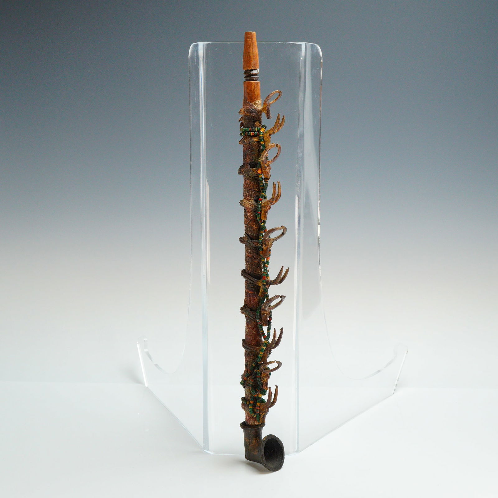 Senufo Traditional Smoking Pipe: This Senufo traditional smoking pipe is constructed from wood, bronze, beads, and snake exudate. The long wooden stem is wrapped in a textured fiber material and snake exudate, featuring multiple